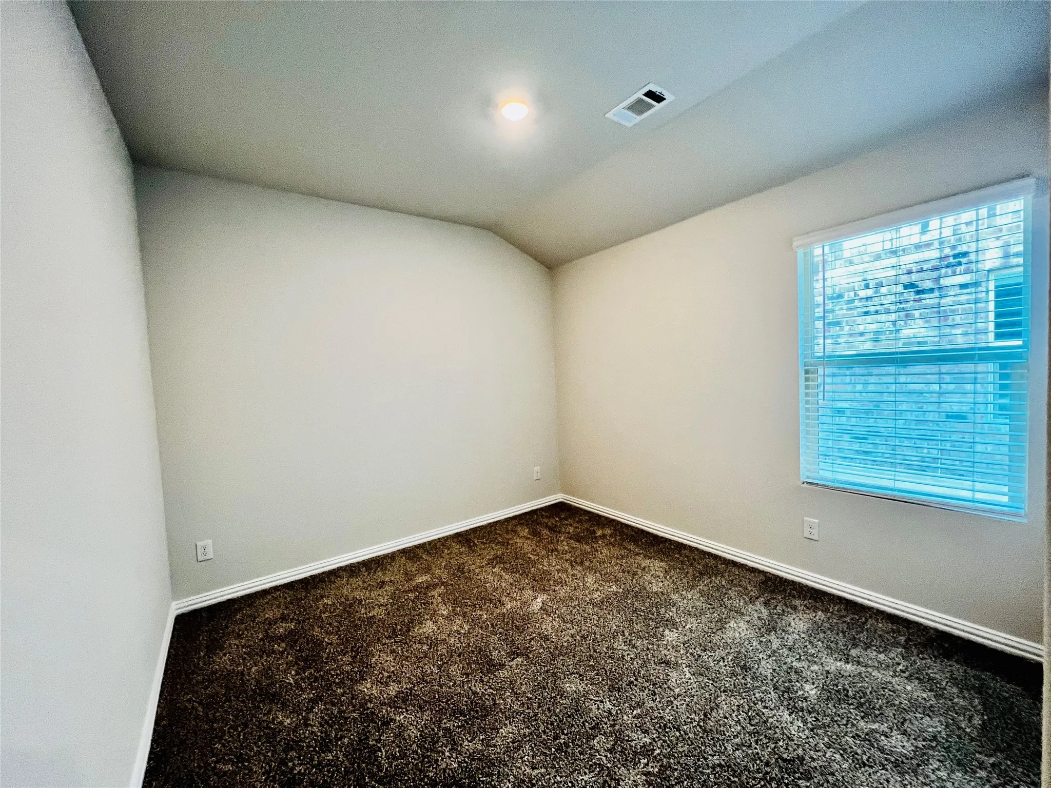 Neutral tone wall paint, textured carpeting, recessed ceiling light, and a window with blinds