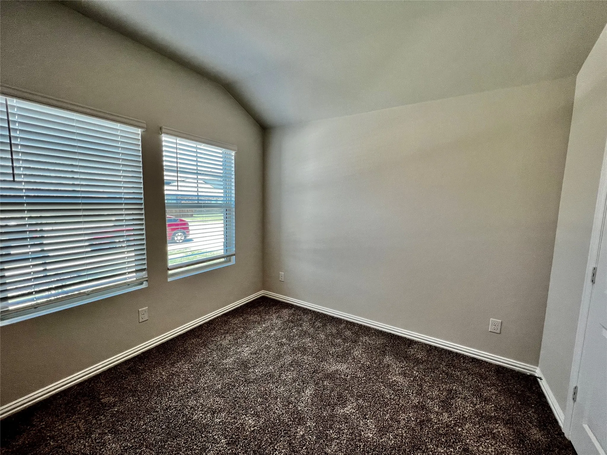 Vaulted ceiling, two windows, horizontal blinds, neutral wall paint, and dark pile carpeting