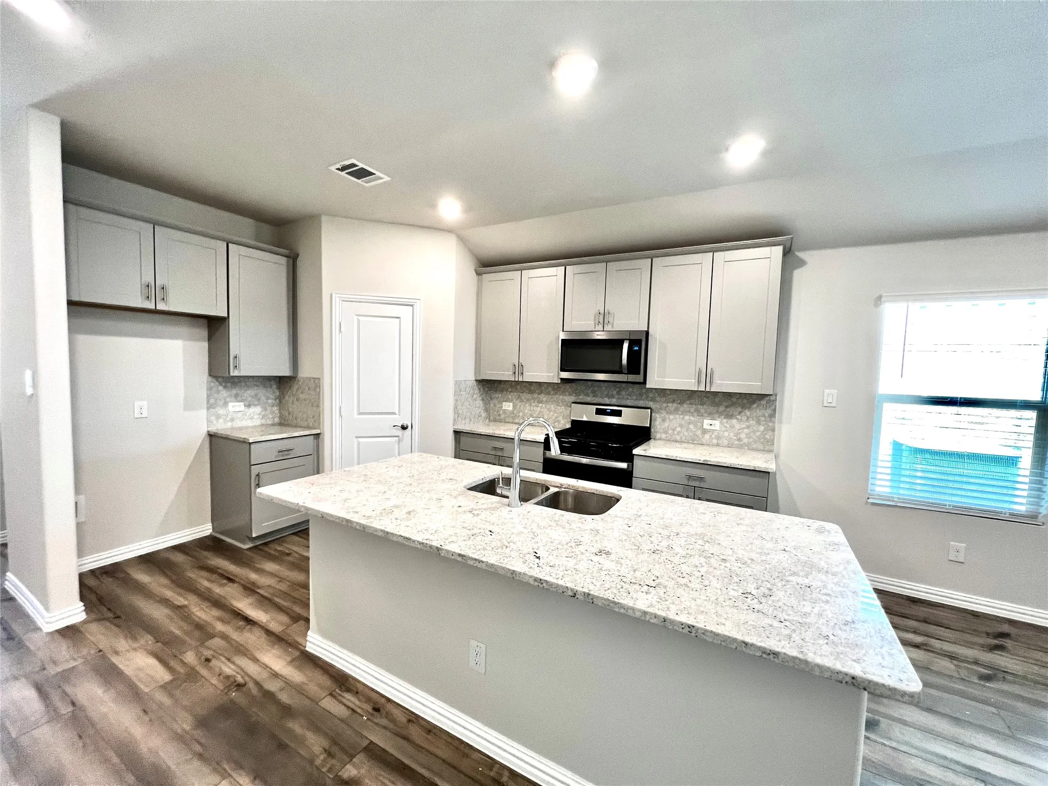 Kitchen featuring an island with an undermount dual-basin sink, light-toned countertops, wood-finish flooring, and gray cabinetry