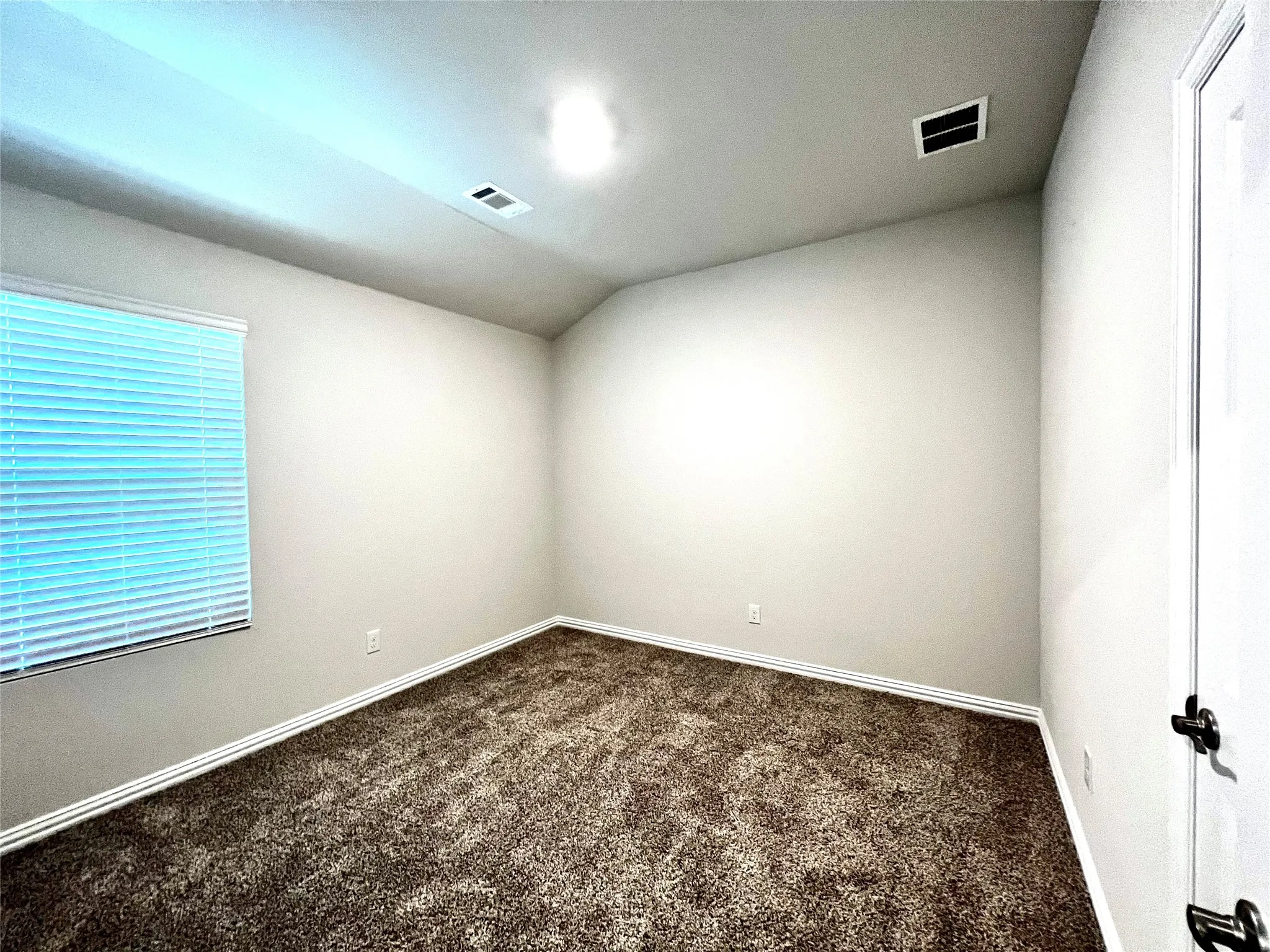Neutral wall finishes, textured carpet flooring, window with horizontal blinds, and a white interior door with dark hardware