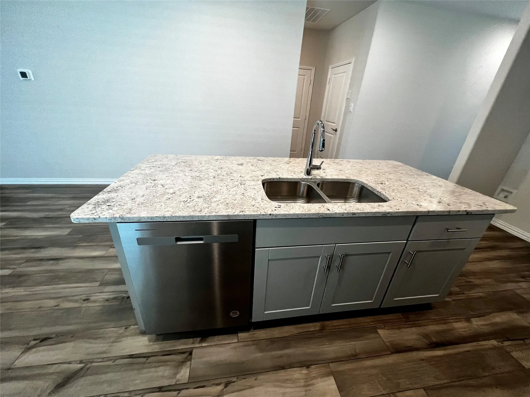 Kitchen island with a light-colored countertop, stainless steel sink, contemporary faucet, stainless steel dishwasher, and wood-finish flooring