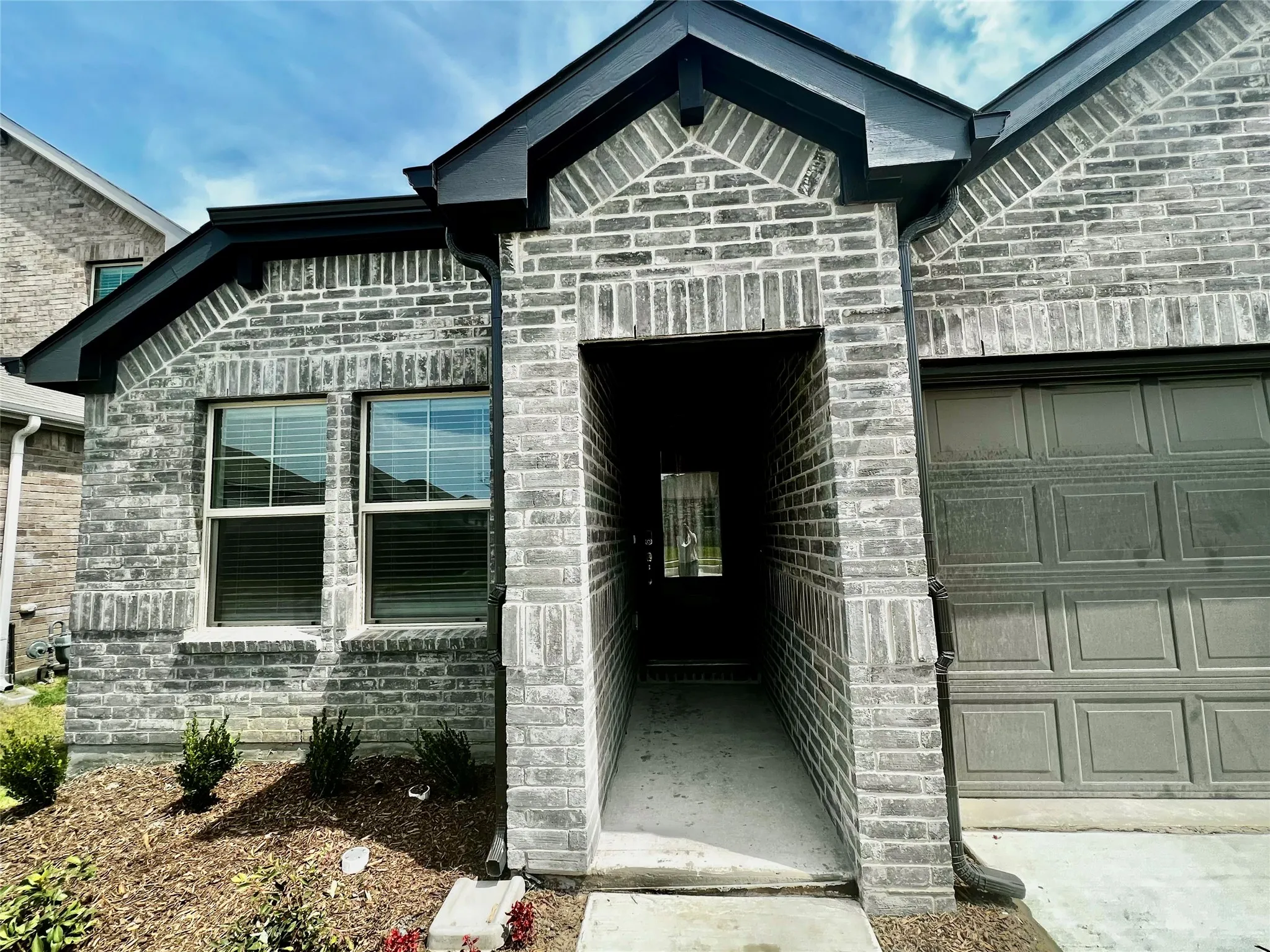 Brick exterior with dark trim accents, covered entry, and attached garage