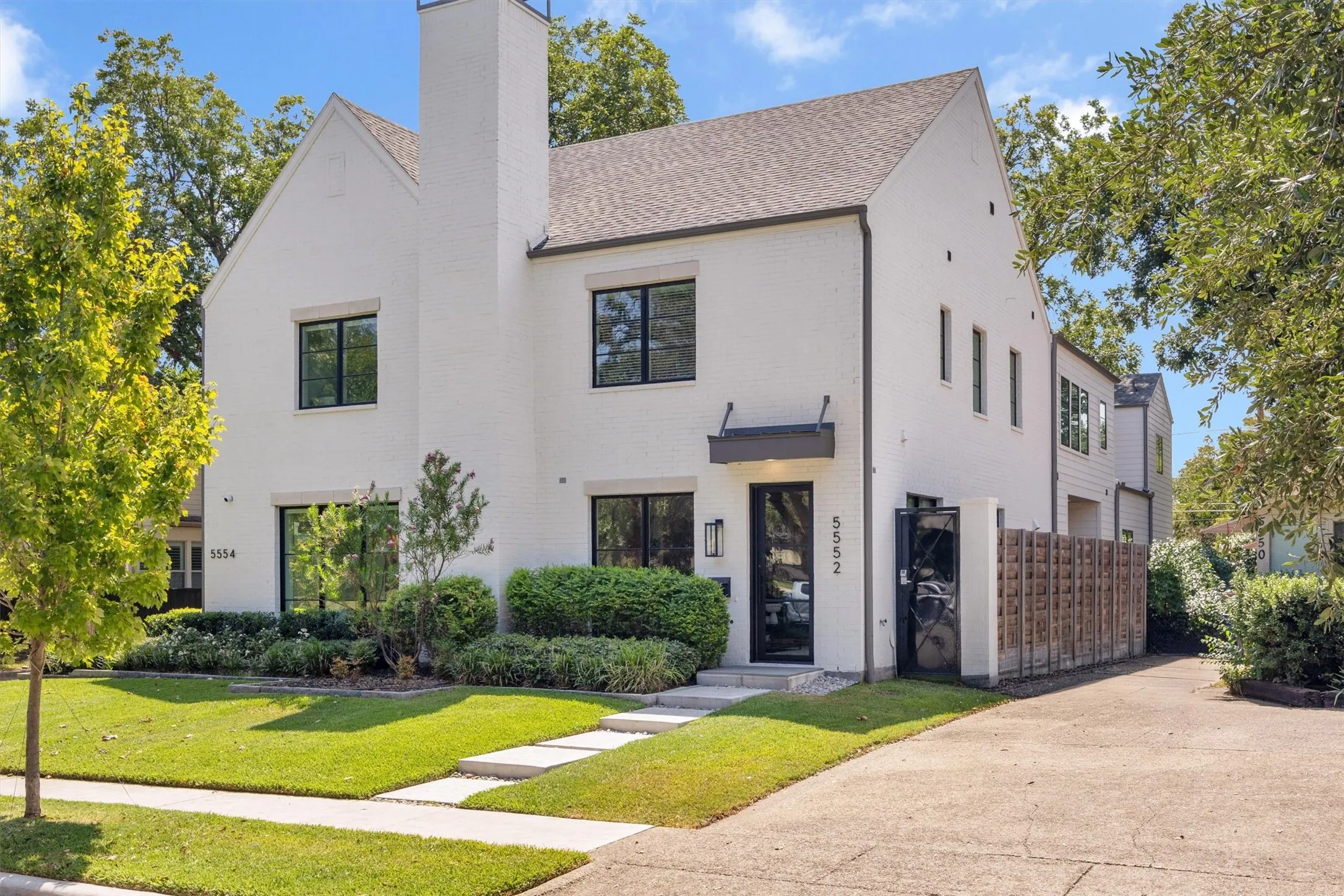 Clean lined, fresh looking exterior of painted brick, iron & glass front door, professional mature landscaping.