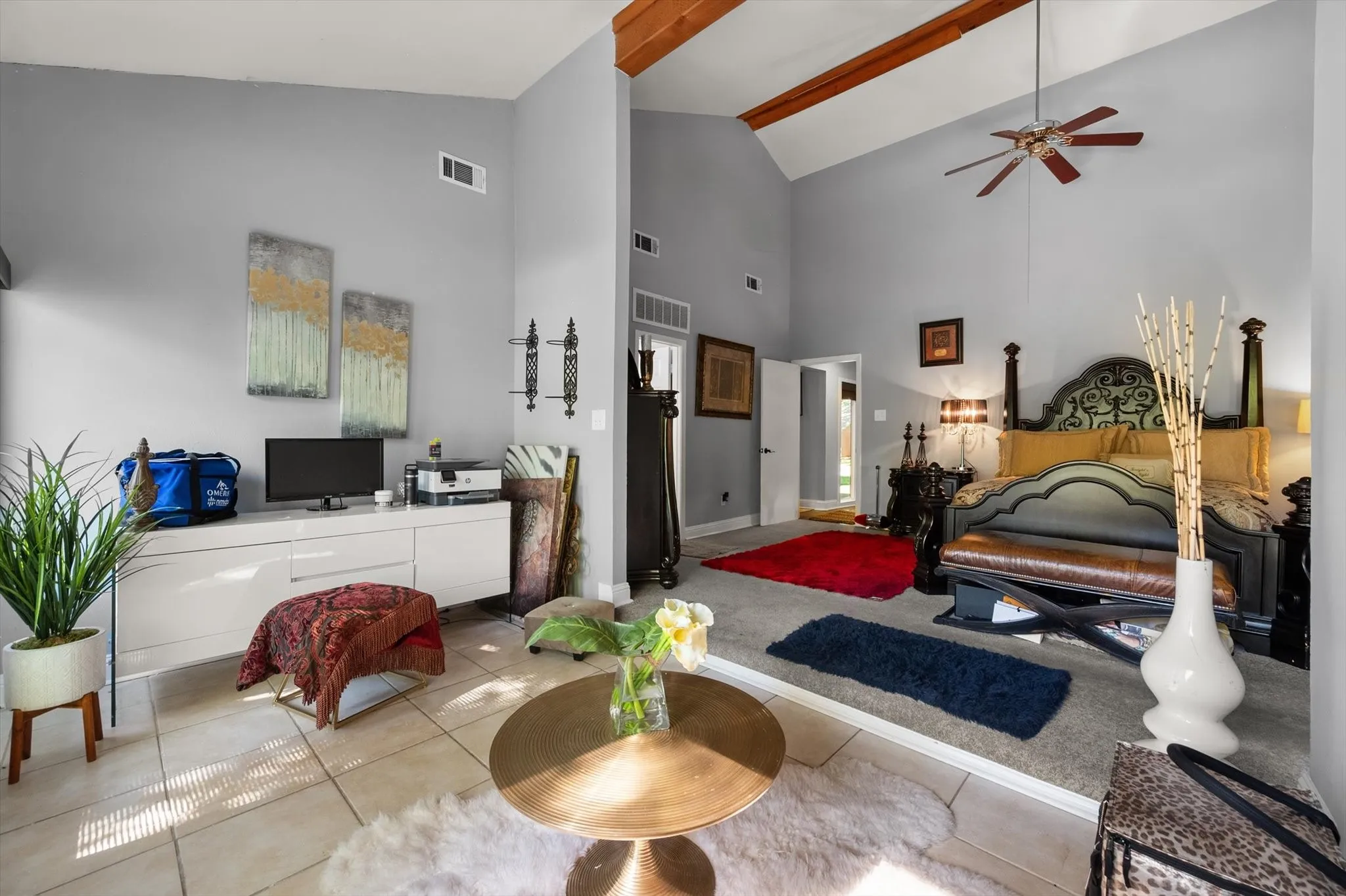 Vaulted ceiling with exposed wood beams, ceiling fan, tile flooring, and a raised carpeted area