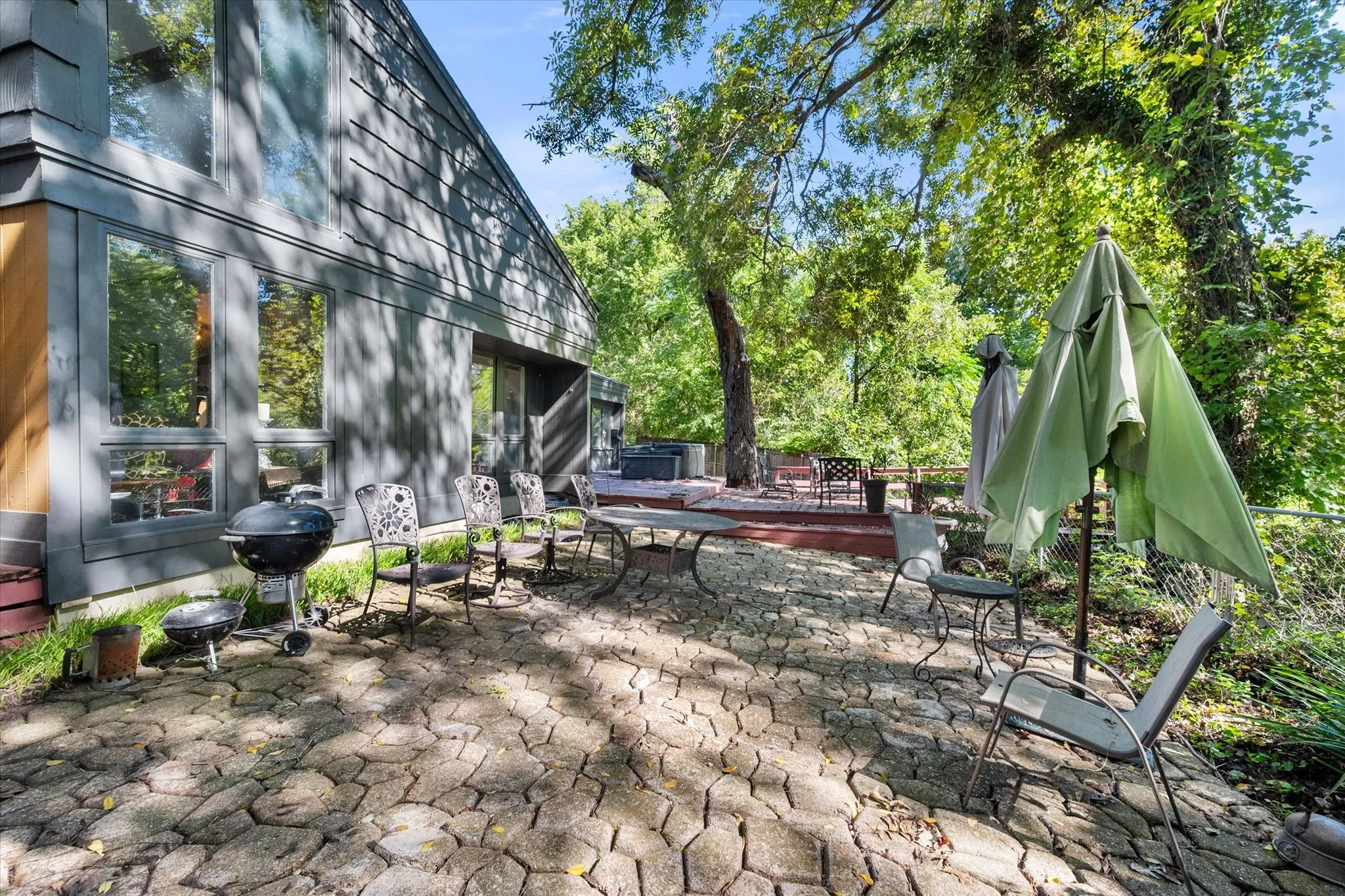 Exterior featuring large windows, gray siding, a stone paver patio, and a raised wood deck