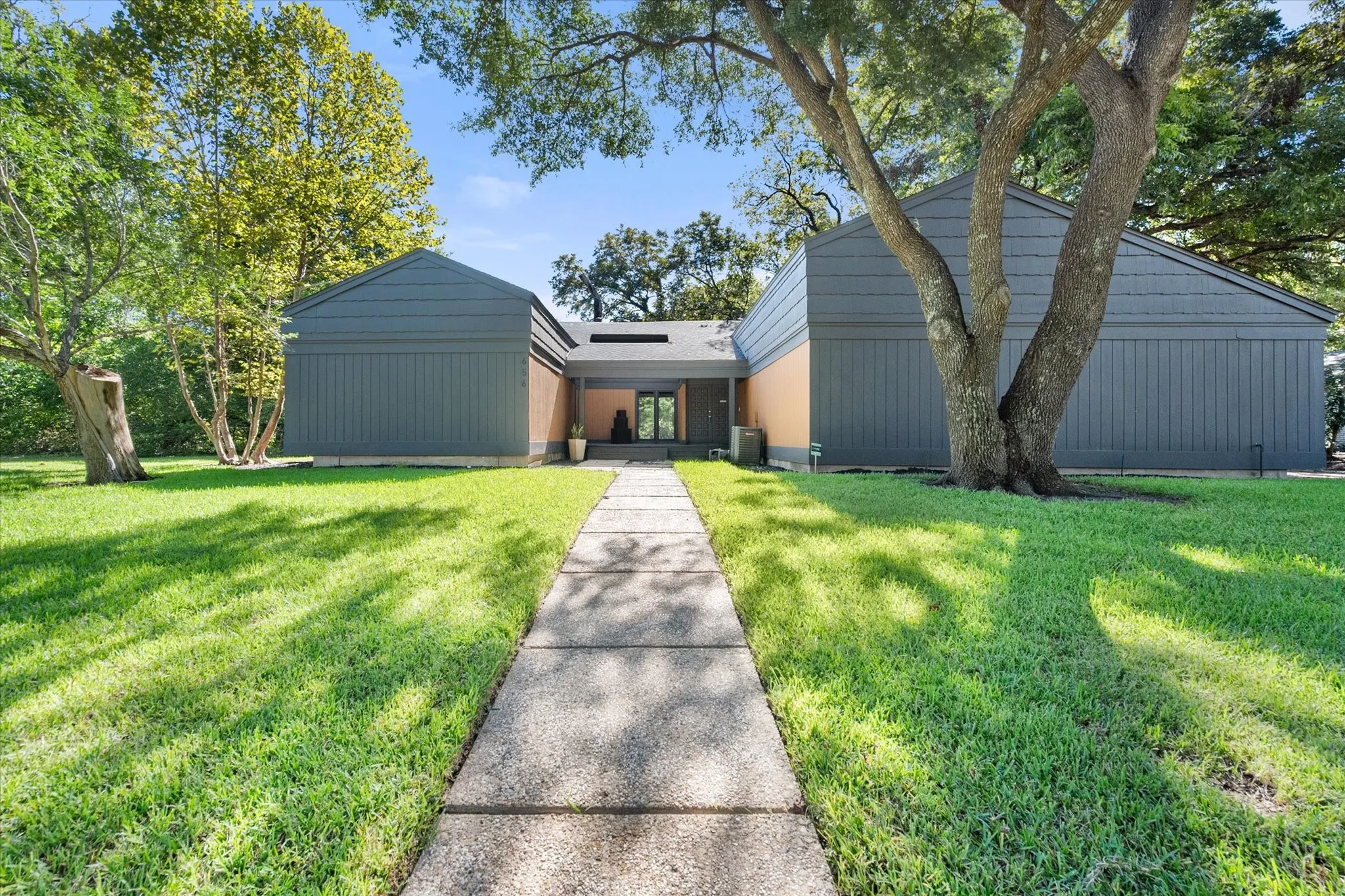Modern exterior with a central entryway, a concrete walkway, and surrounding green lawn
