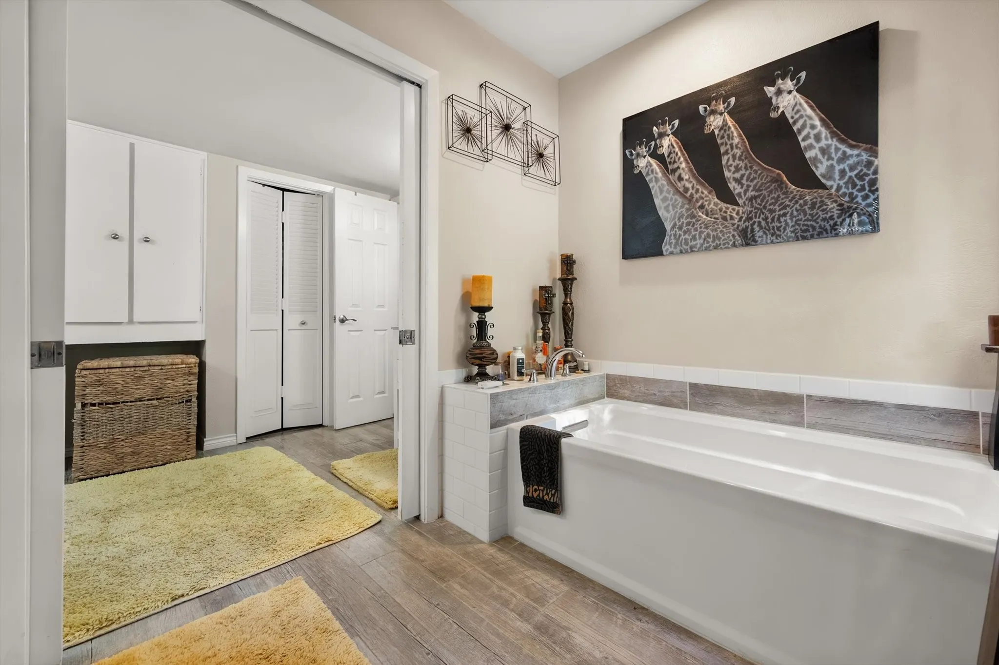 Built-in tub with tile surround, wood-finish flooring, and white storage cabinetry