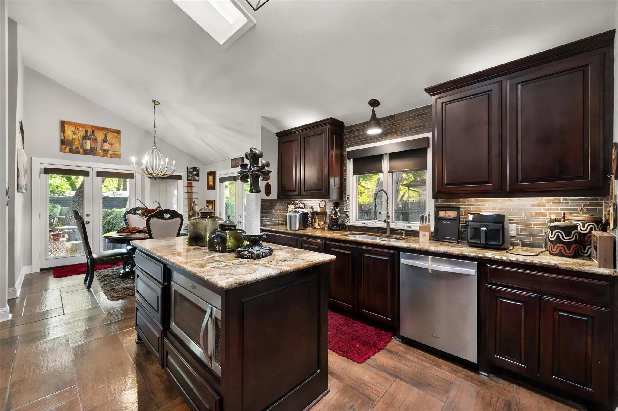 Kitchen featuring dark wood cabinetry, a central island with a built-in microwave, stainless steel appliances, and a skylight