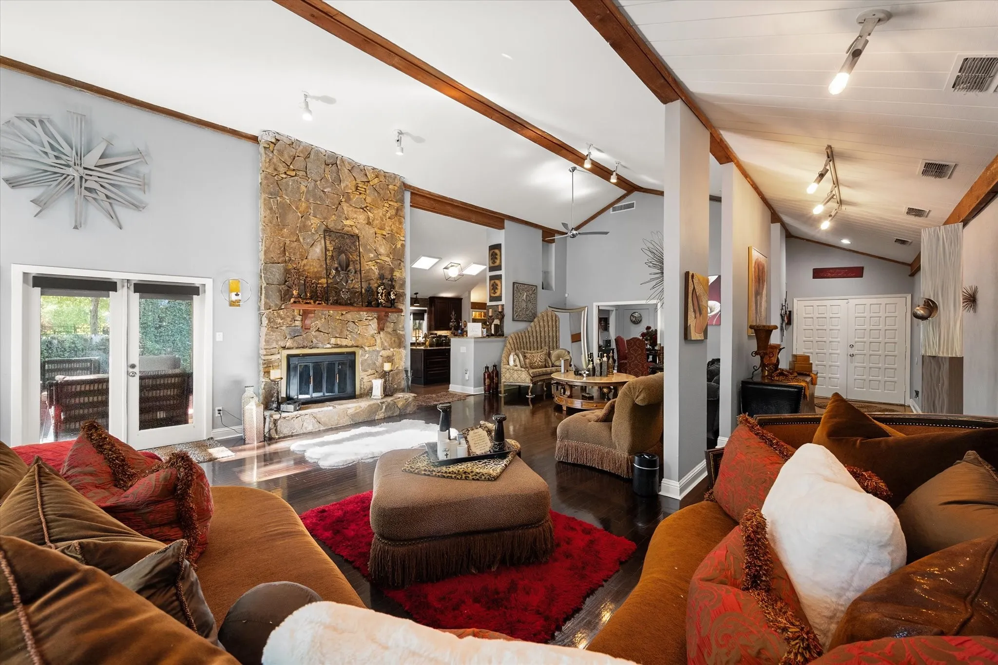 Vaulted ceilings with exposed wood beams, stone fireplace, dark wood-finish flooring, and double patio doors