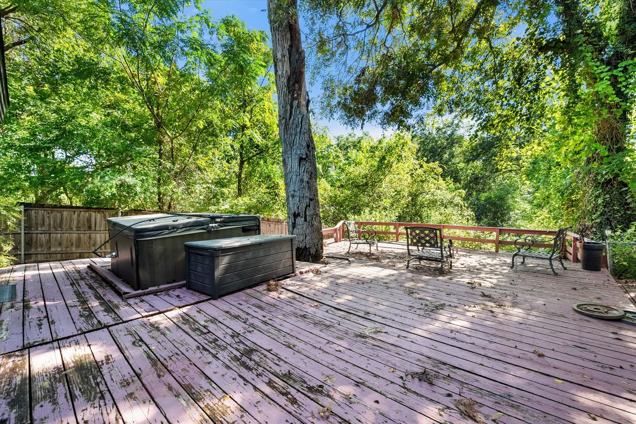 Expansive wood deck with a built-in hot tub, surrounded by mature trees, and featuring a wood privacy fence