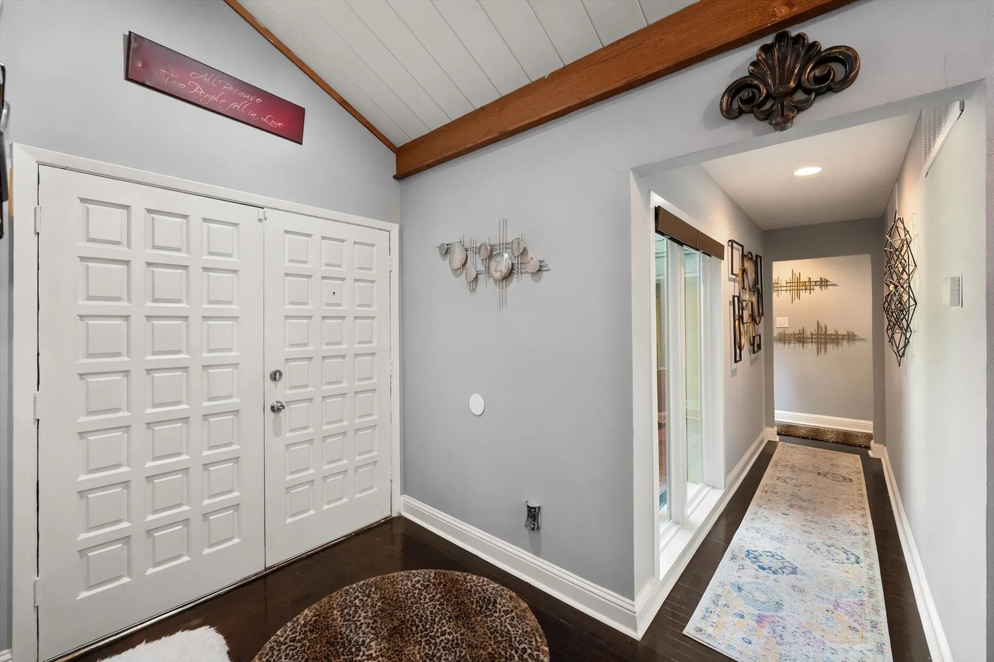 Vaulted wood-paneled ceiling with an exposed wood beam, dark wood-finish flooring, and white double entry doors with square paneling