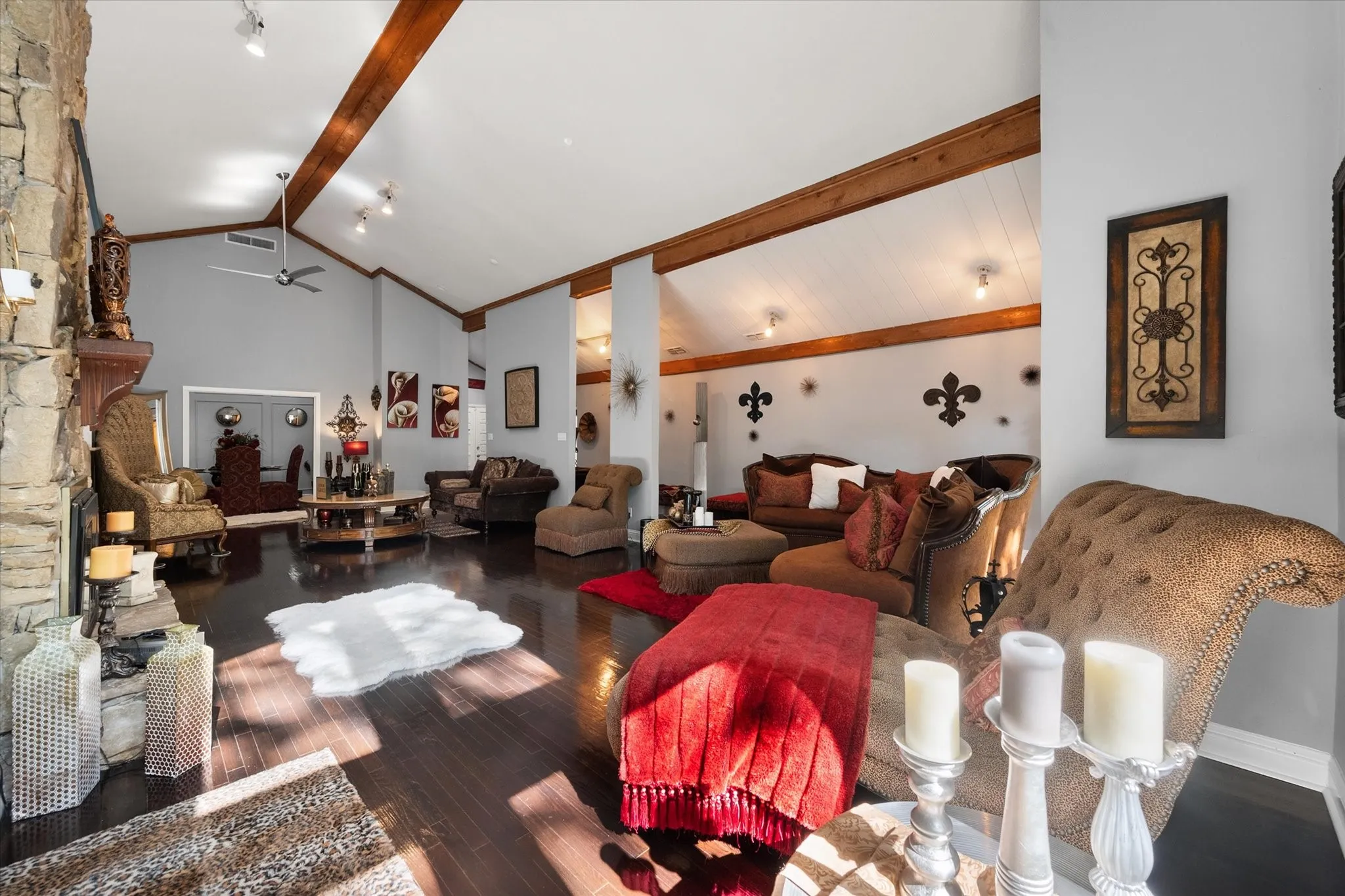 Vaulted ceilings with exposed wood beams, stone-clad fireplace with wood mantel, dark wood-finish flooring, and recessed lighting