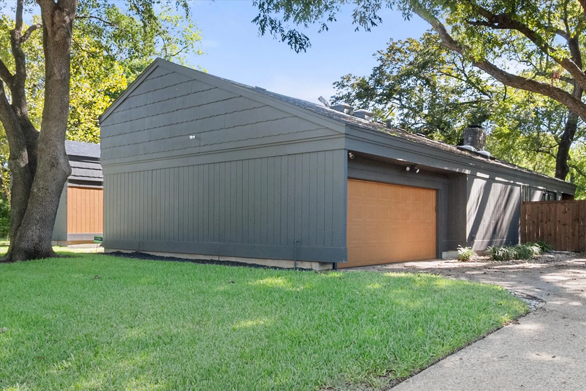 Horizontal siding with vertical paneling accents, light-toned wood-finish garage door, and a partially visible wood privacy fence