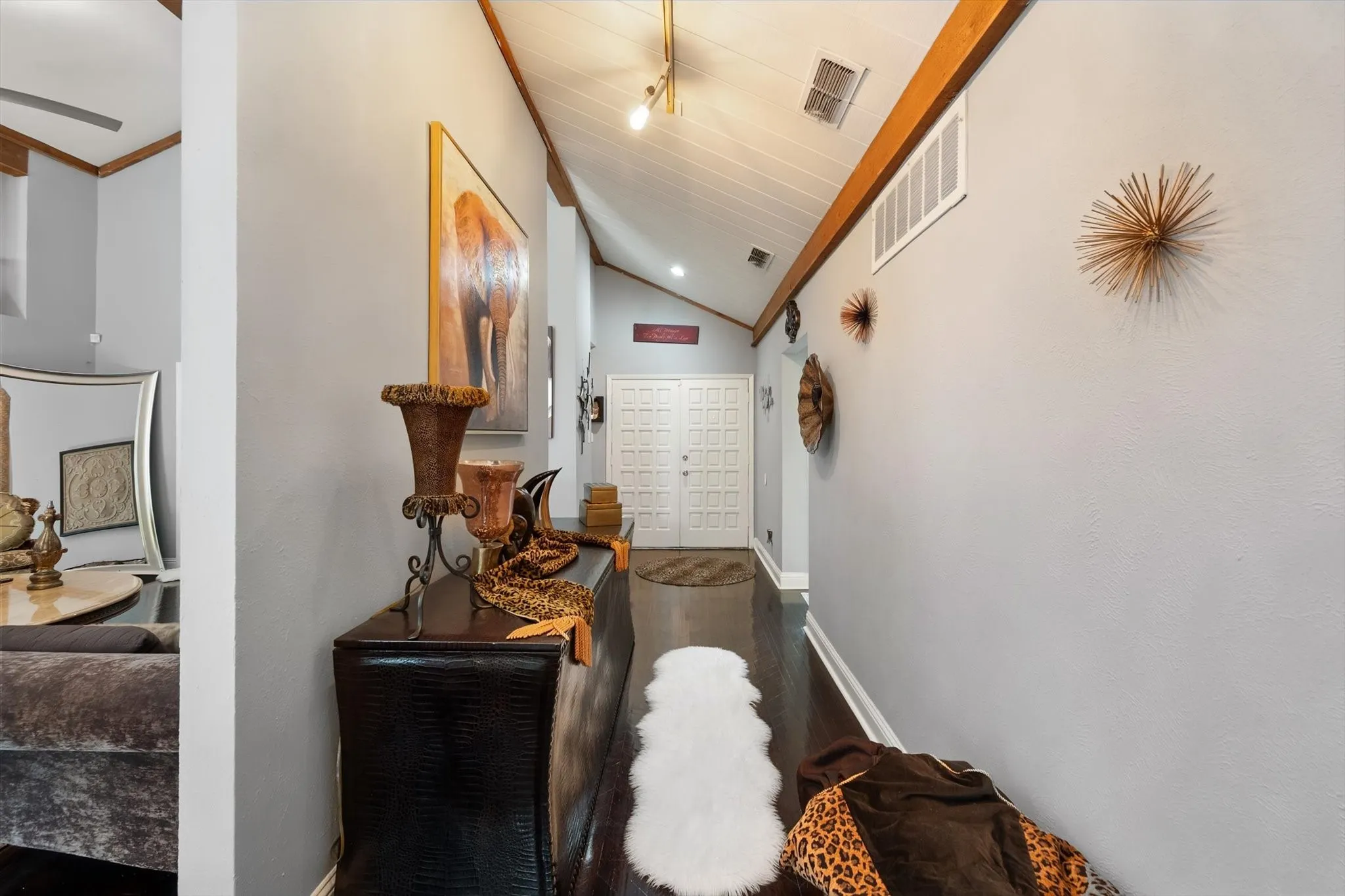 Vaulted ceiling with exposed wood beams, track lighting, wood-finish flooring, and a paneled entry door