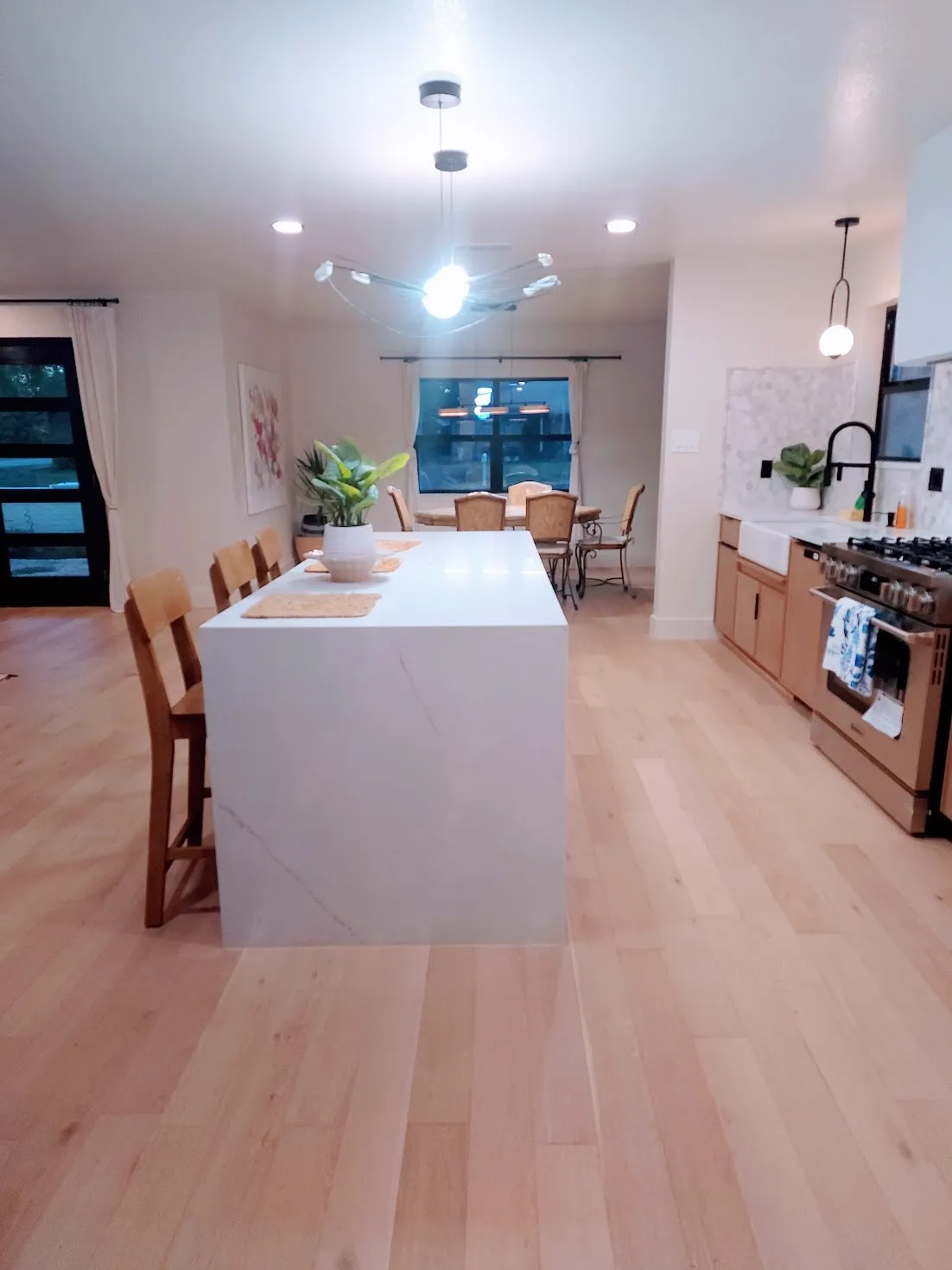 Spacious kitchen featuring a large island with seating, light wood-finish flooring, built-in stainless steel range, and a white farmhouse sink