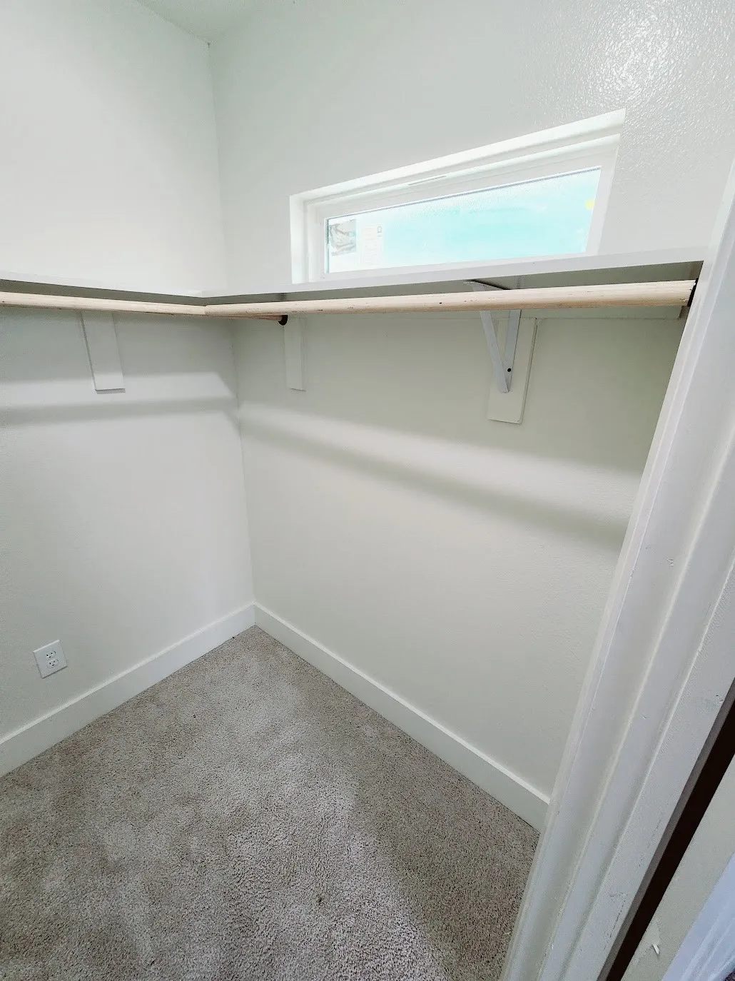 Built-in shelving and hanging rod with a high horizontal window and carpeted flooring