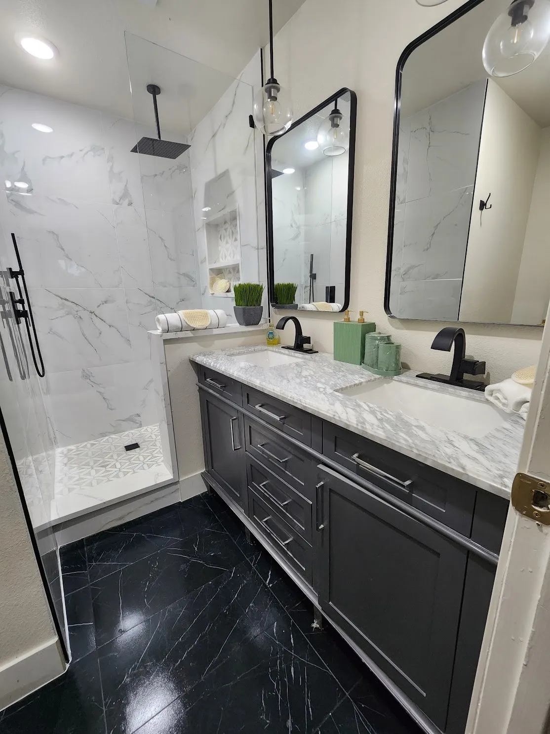 Black marble-look floor tiles, dual vanity with shaker-style cabinetry, two framed mirrors, and a glass-enclosed shower with a rainfall showerhead