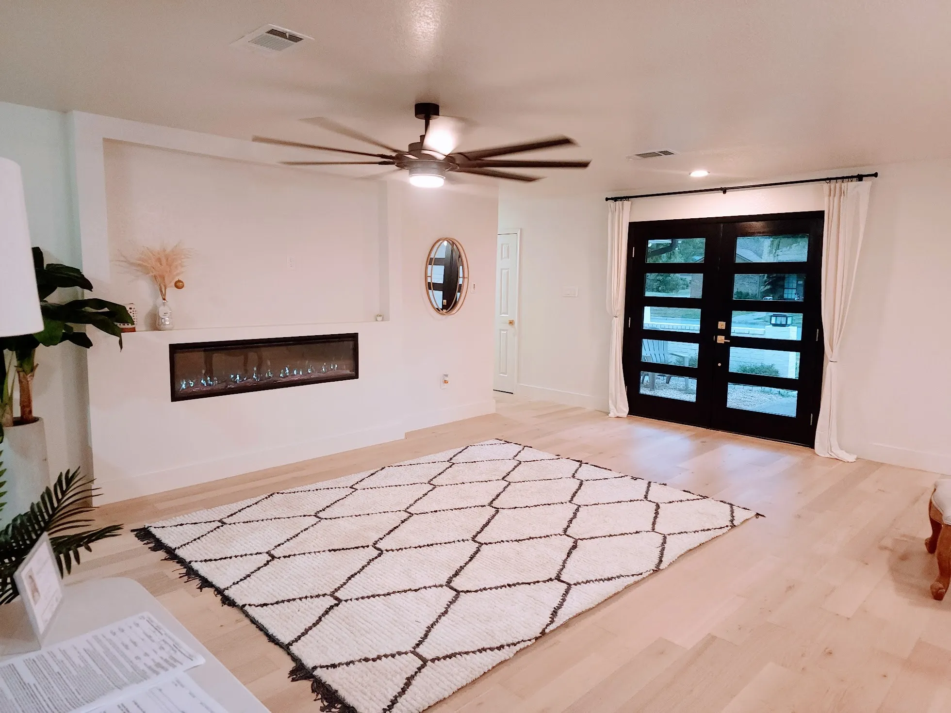 Wood-finish flooring, built-in linear electric fireplace, modern ceiling fan with lighting, recessed lighting, and black framed double entry doors