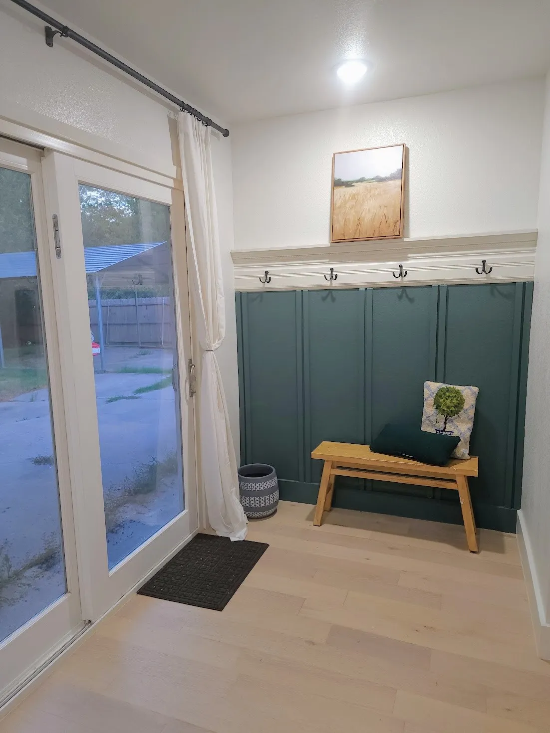 White paneled door with glass inserts, light wood-finish flooring, and a green wainscoting accent wall with integrated coat hooks