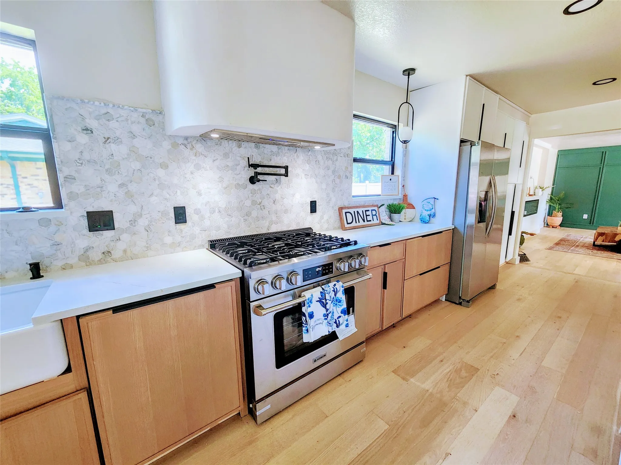 Stainless steel range, white countertops, light wood-finish cabinetry, mosaic tile backsplash, and light wood-finish flooring