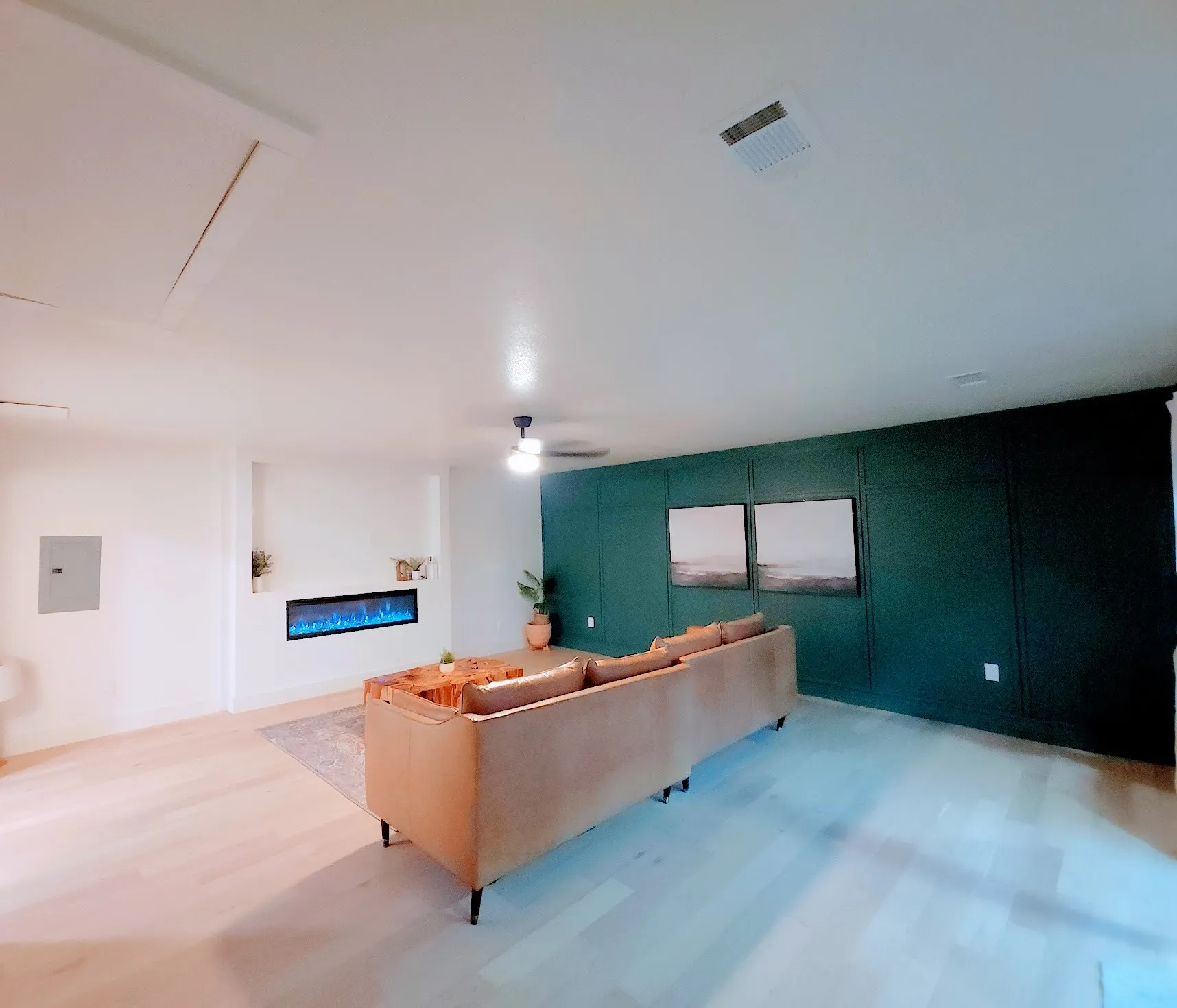 Light wood-finish flooring, recessed electric fireplace, dark green accent wall with paneling, and a ceiling fan with integrated lighting