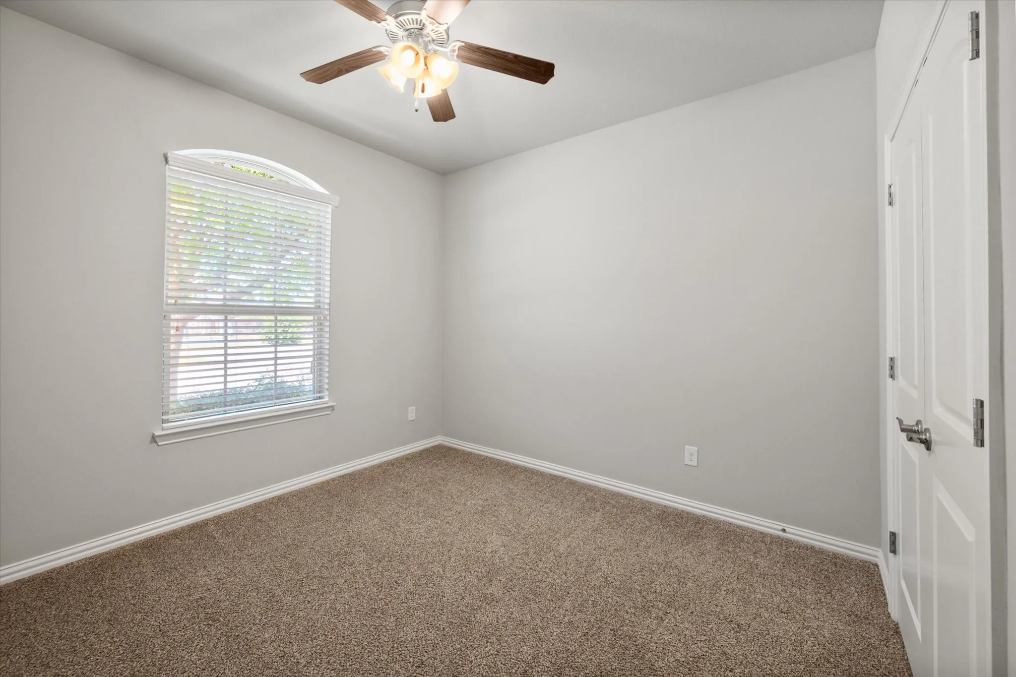 Private secondary bedroom in a thoughtfully designed split-bedroom floor plan, offering excellent privacy from the primary suite. The spacious room features plush carpeting, fresh neutral paint, an abundance of natural light through an elegant arched-top window, ceiling fan and generous wall space for flexible furniture placement.