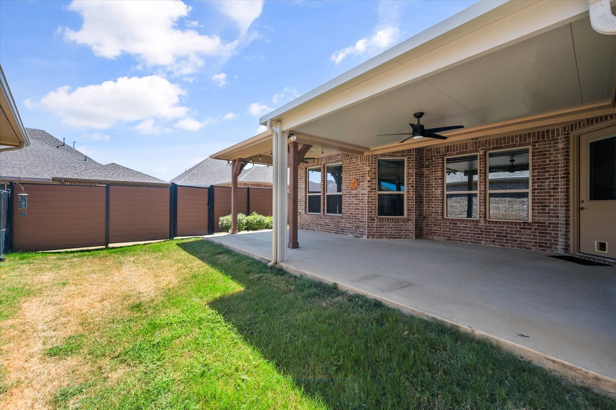 Backyard retreat featuring an oversized covered patio with a ceiling fan, spacious grassy area, and a privacy fence—an ideal setting for outdoor entertaining, relaxing, and enjoying Texas evenings.