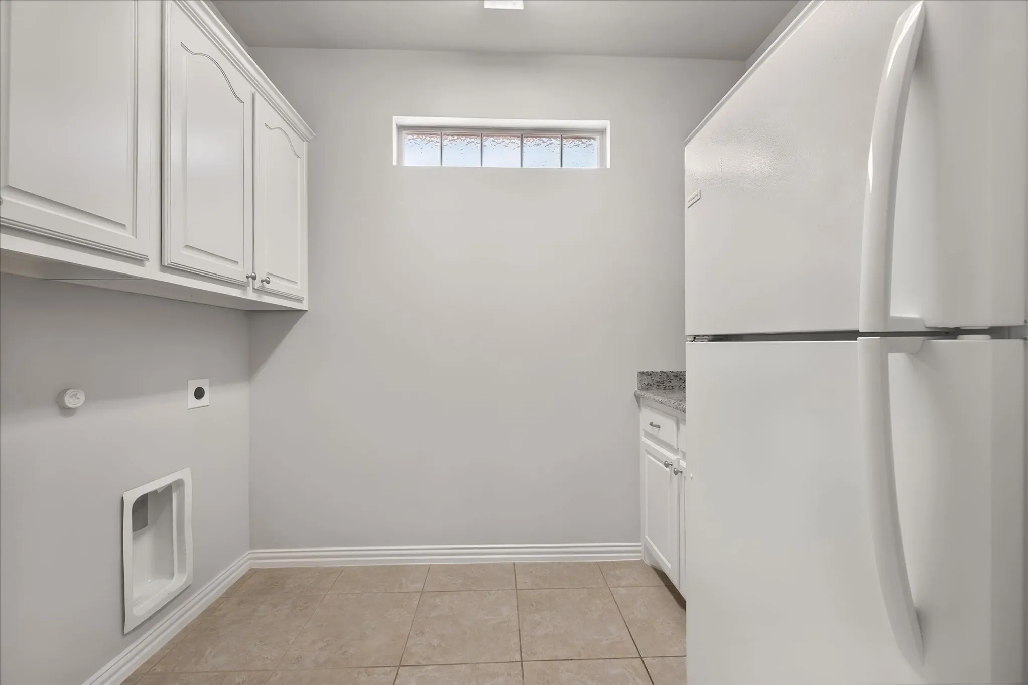 Large laundry room has built in cabinets, ceramic tile flooring, a sink space with room for additional refrigerator.