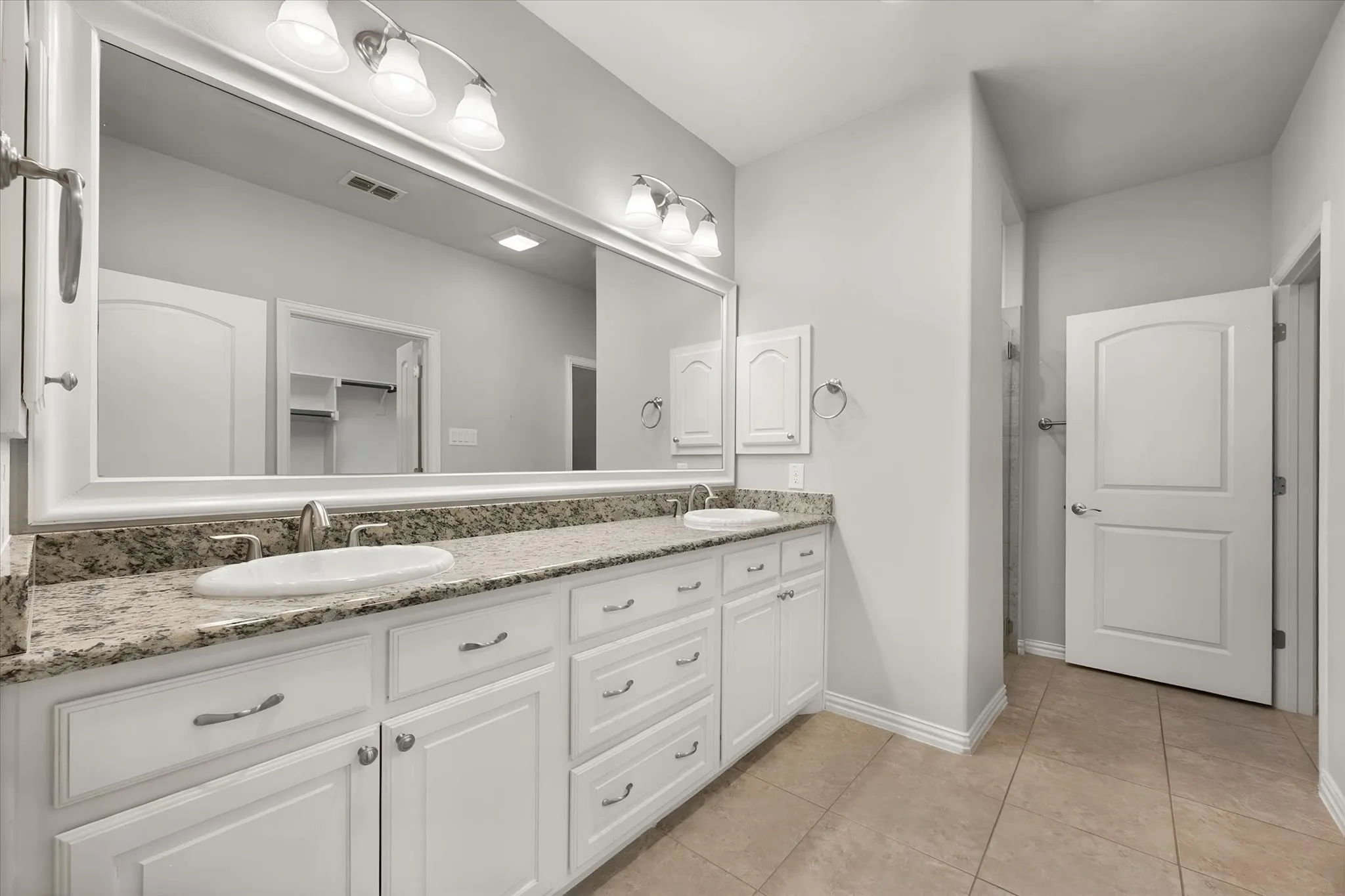 Primary bathroom featuring white shaker cabinetry, granite countertops, dual sinks, oversized vanity, tile flooring, and a spacious walk-in shower.