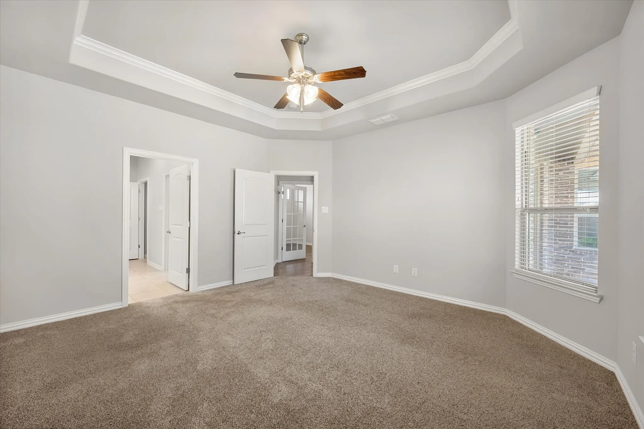 Spacious primary bedroom featuring a tray ceiling, ceiling fan, plush carpeting, and abundant windows that fill the room with natural light. Split bedrooms for privacy.