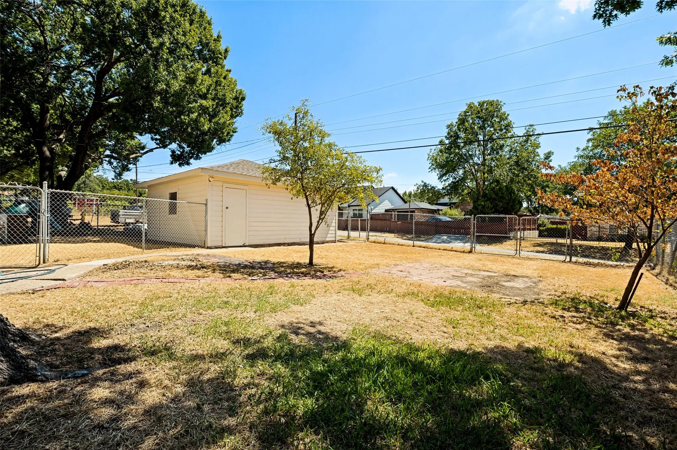 Detached outbuilding with horizontal siding and a composition shingle roof, accompanied by a chain-link fence