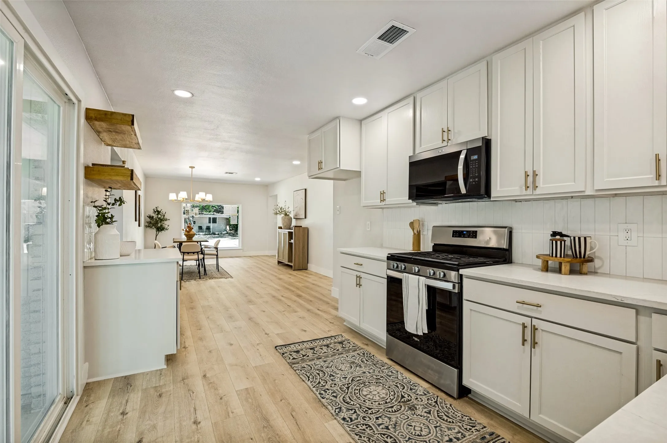 White shaker cabinetry, stainless steel appliances, light wood-finish flooring, white countertops, and sliding glass doors