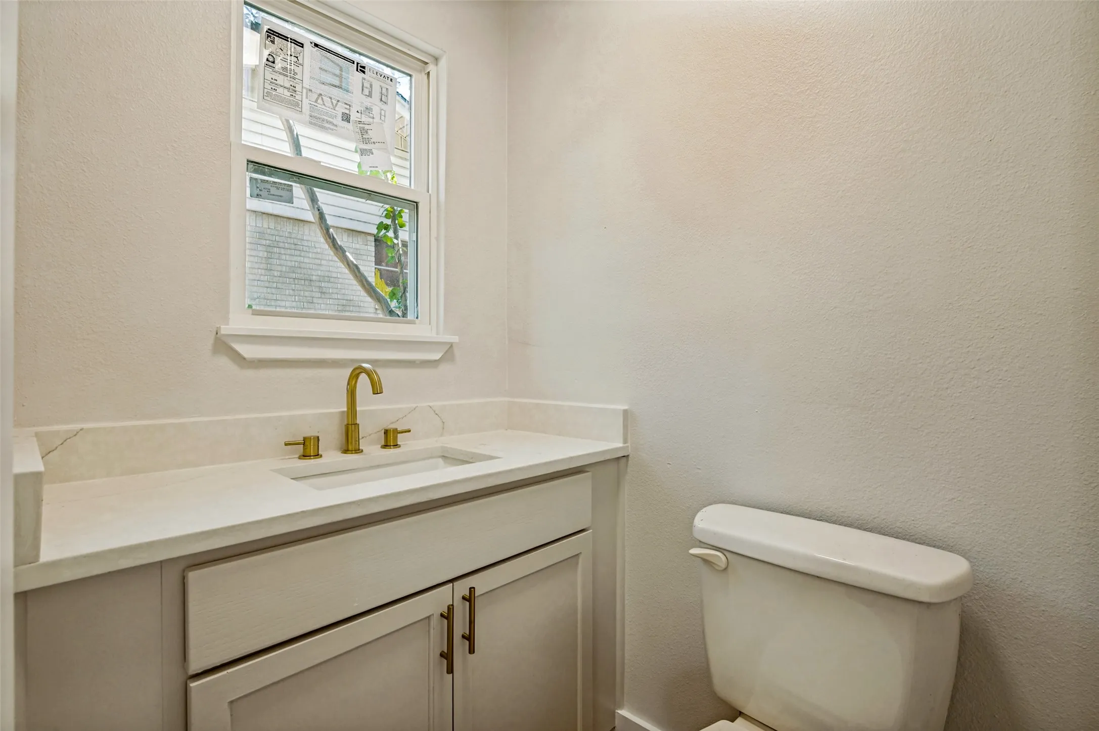 Vanity with an integrated rectangular sink, gold-finish faucet, and a light-toned countertop