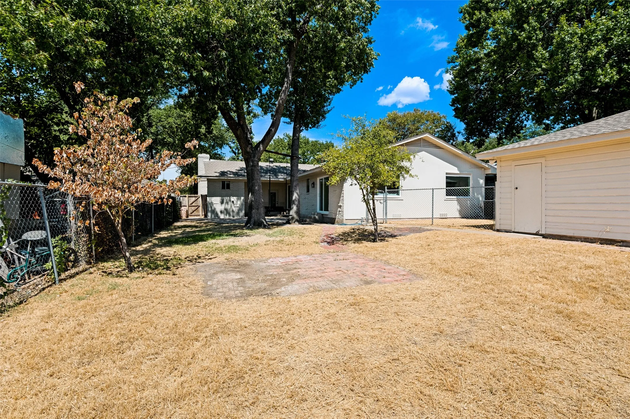Expansive backyard with mature trees, chain-link fencing, and a detached storage shed