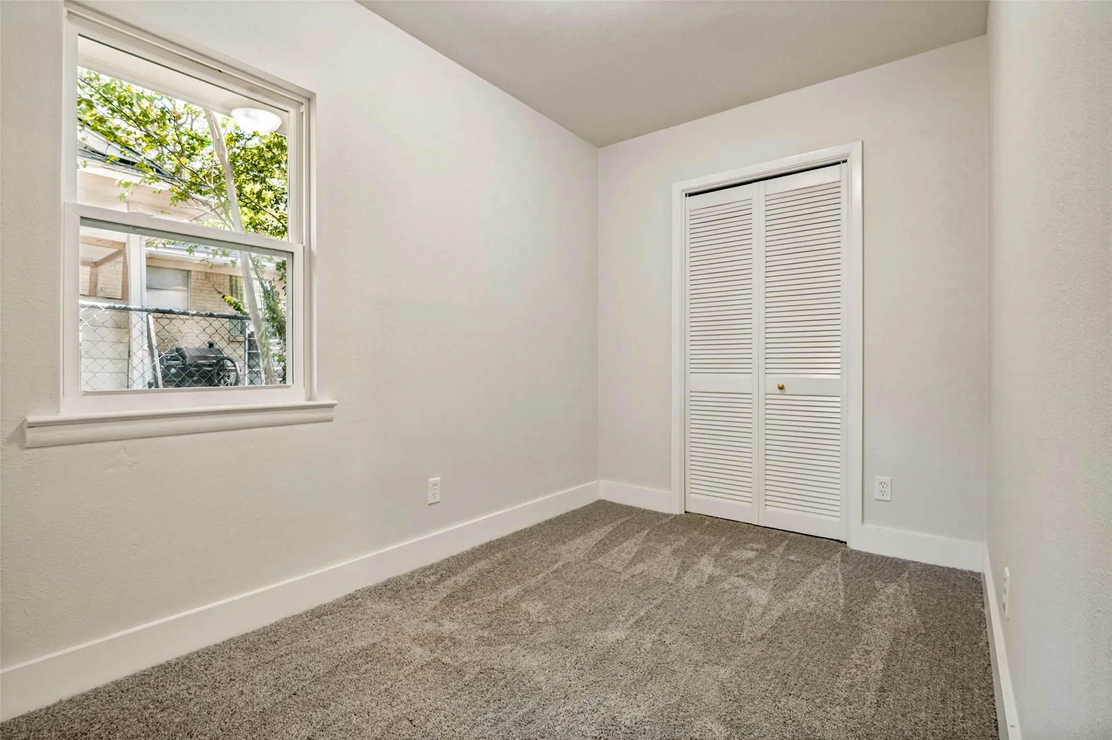 Gray carpet flooring, white walls, double-hung window, and bi-fold louvered closet doors