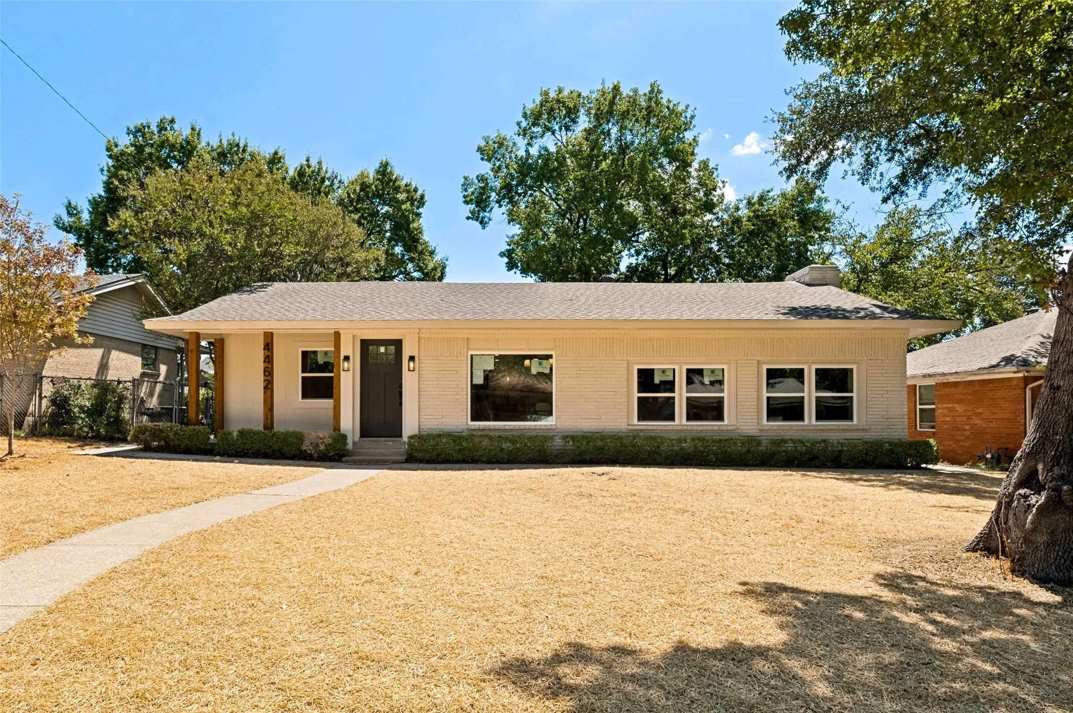 Light-colored brick exterior with a dark entry door, wood-tone support columns, and multiple windows