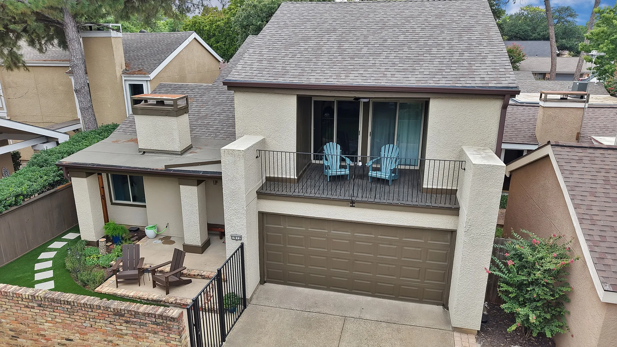 Aerial front exterior — Overhead view showing balcony with seating, covered front porch with paver walkway, and two car garage.