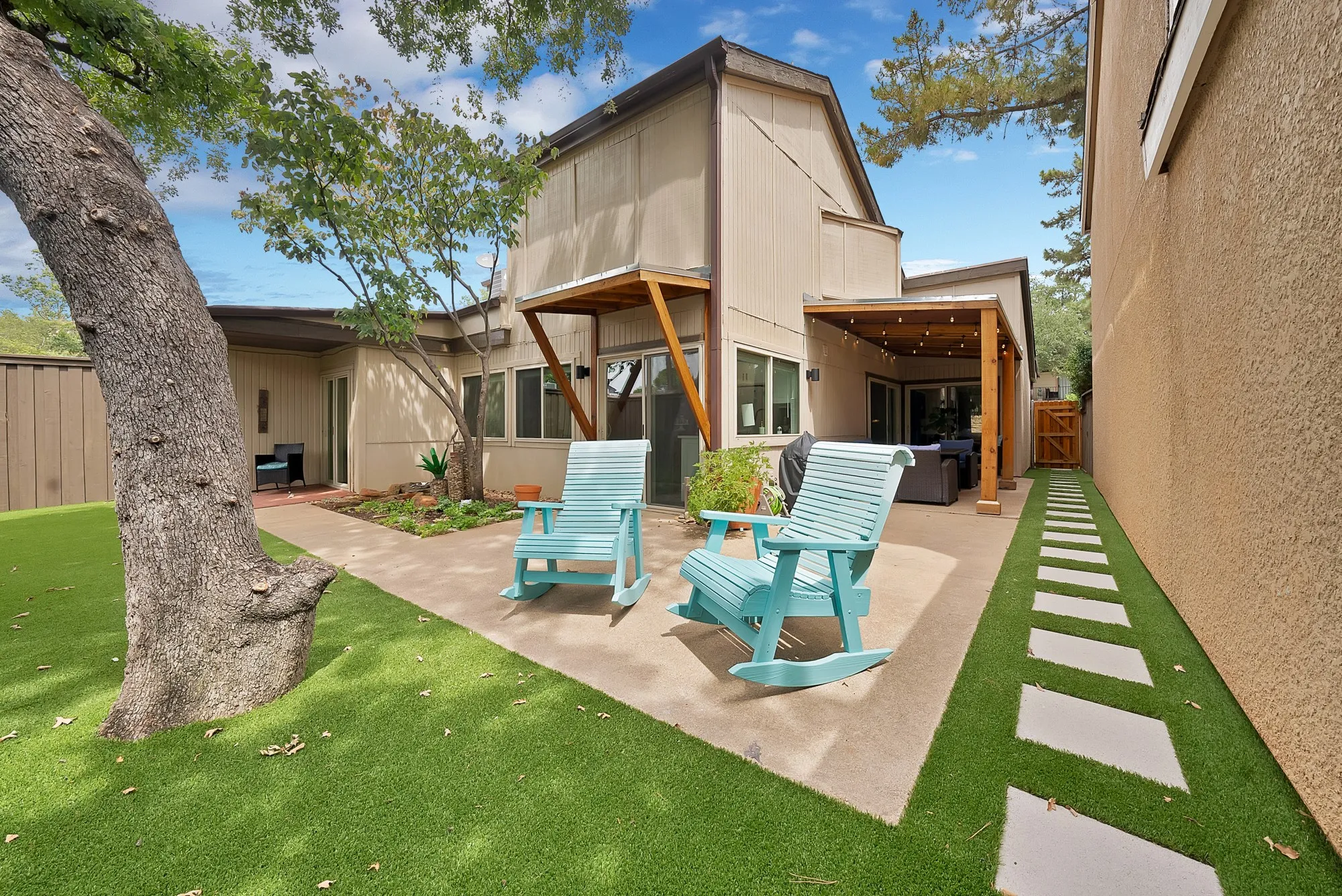 Rear exterior — Two story home with covered patio, string lights, turf lawn, and paver stepping stone path along stucco wall.