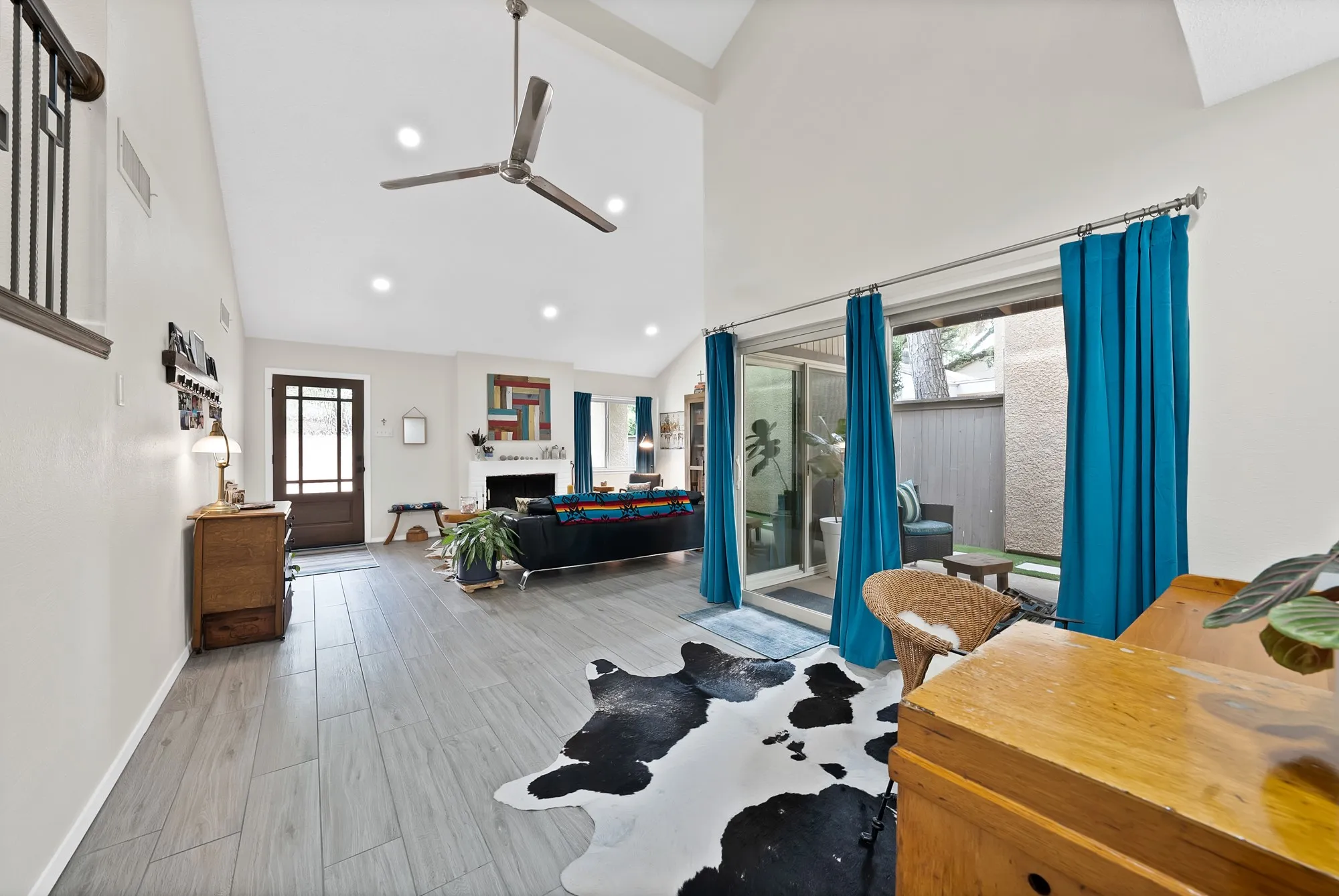 Living room — Vaulted ceiling with sliding glass door to patio, teal curtains, and view through to entry.