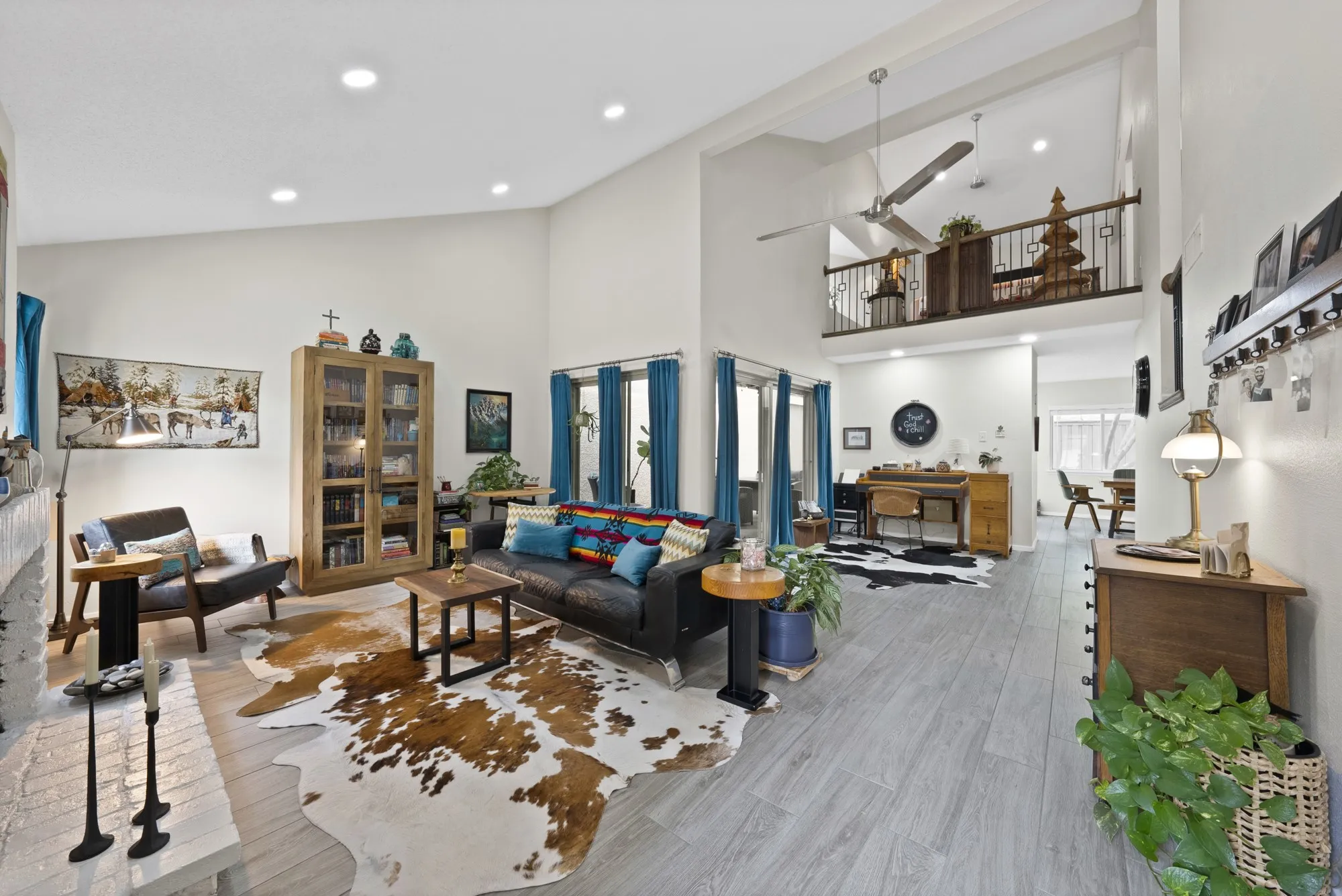 Living room — Vaulted ceiling with exposed wood beam accent, ceiling fan, and open loft overlook above. Wood look tile flooring throughout.