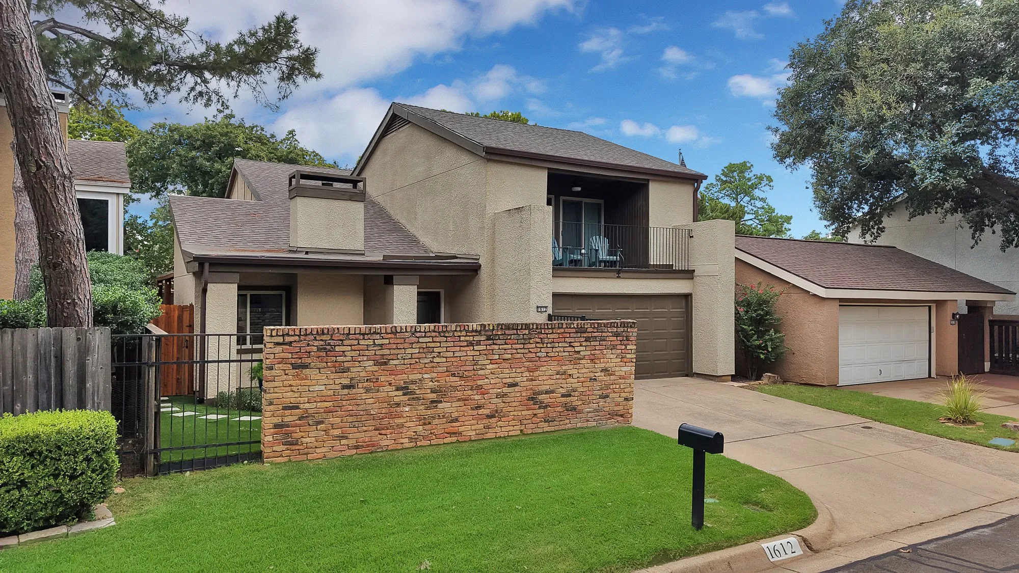 Front exterior — Side angle view of stucco and brick facade with vaulted roofline, chimney, and second floor balcony.