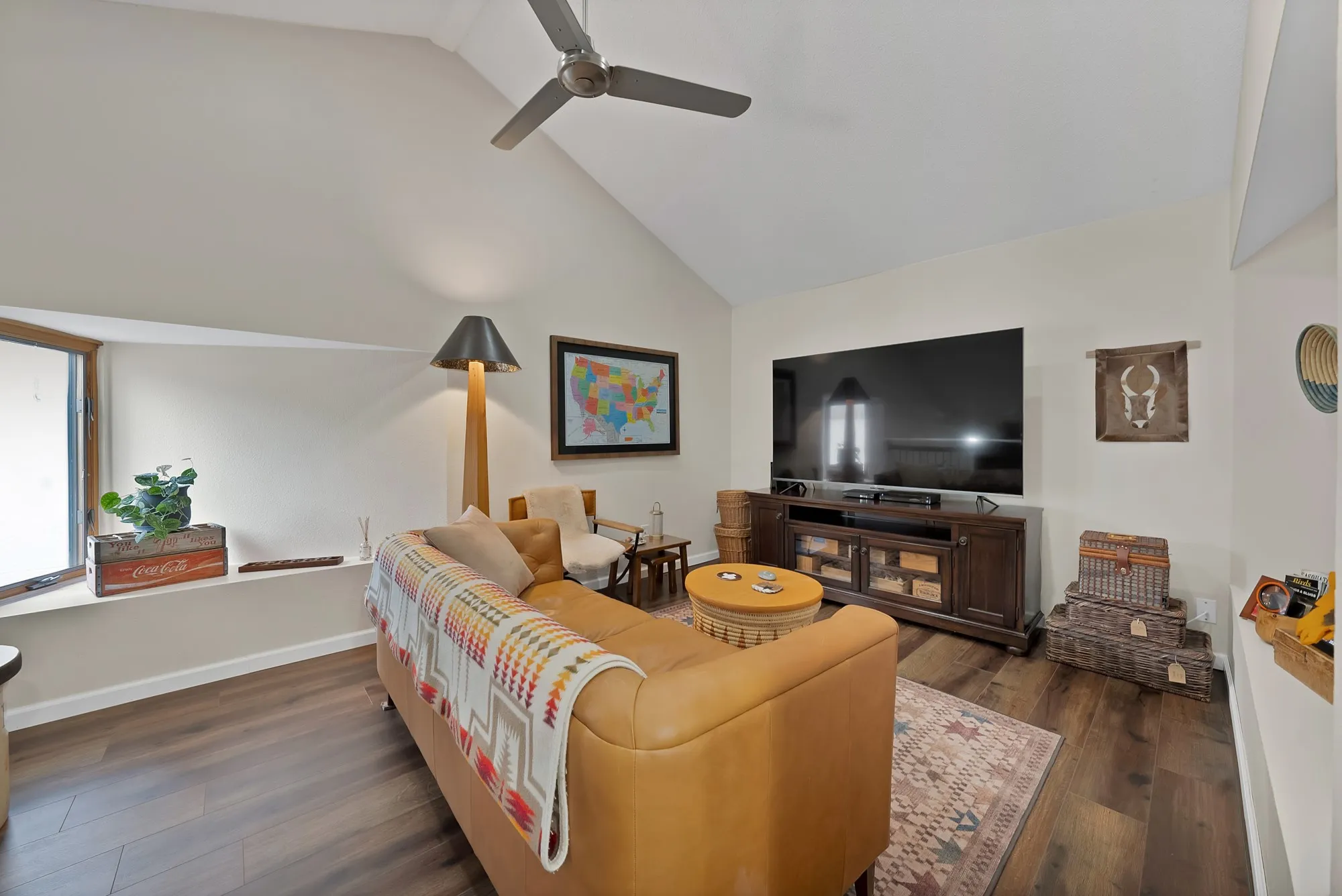 Upstairs loft living area — Vaulted beam ceiling with ceiling fan, large window, and open sightline to stair railing below.