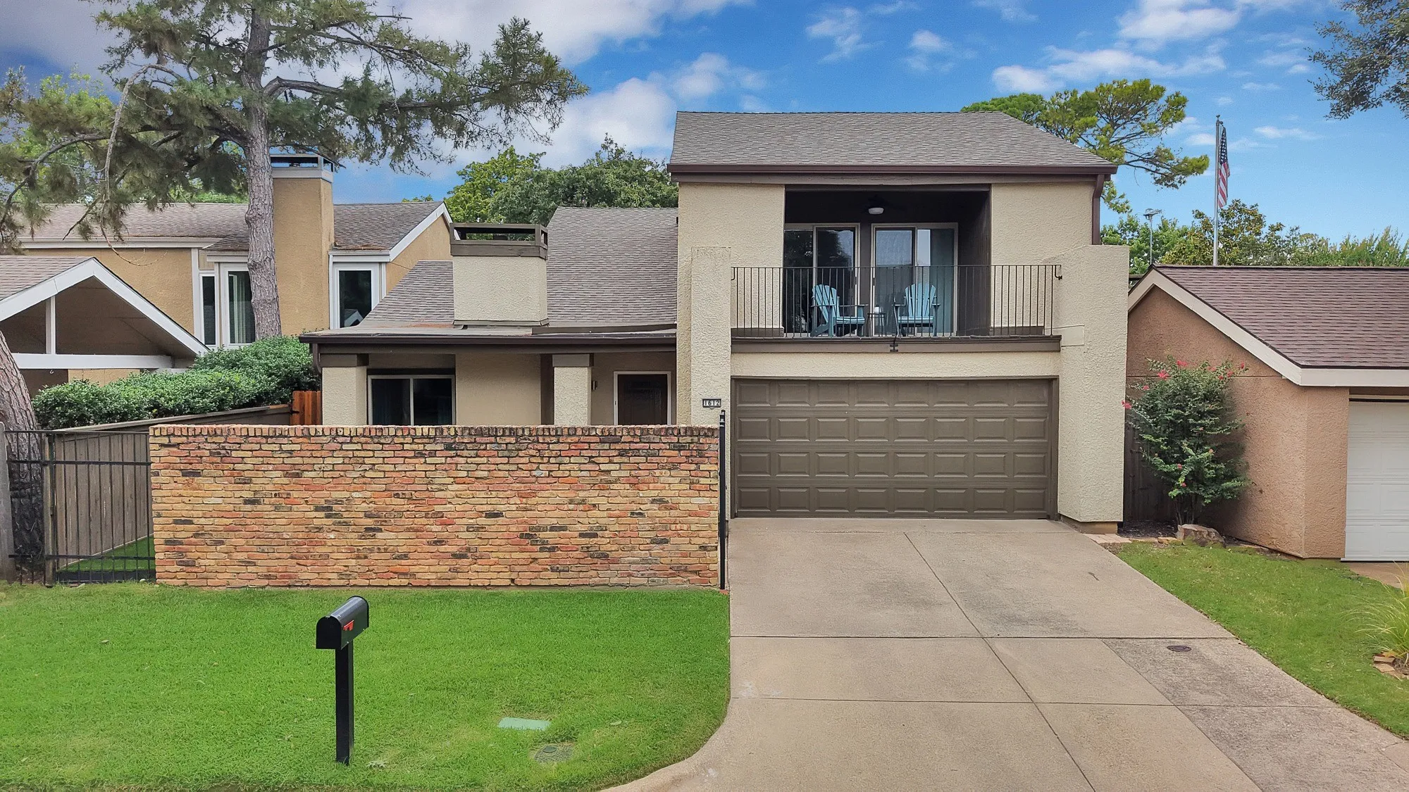 Front exterior — Two story stucco home with brick privacy wall, second floor balcony with iron railing, and attached two car garage.