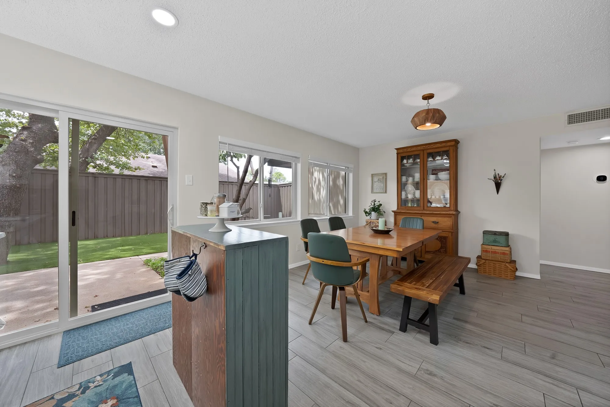 Dining and kitchen — Wood look tile flooring flows from dining area into kitchen, with built-in china cabinet and white shaker cabinetry visible.