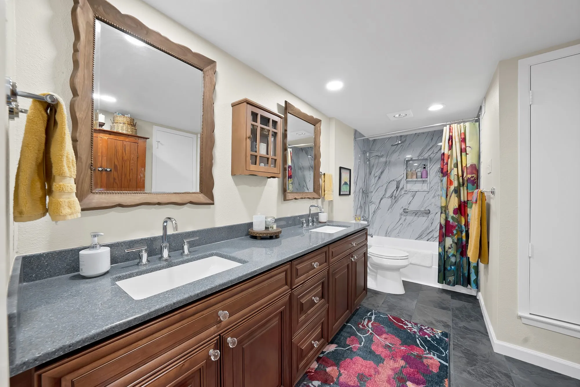 Primary bathroom — Dual vanity with blue solid surface countertop, dark wood cabinetry, and marble tile tub and shower surround.