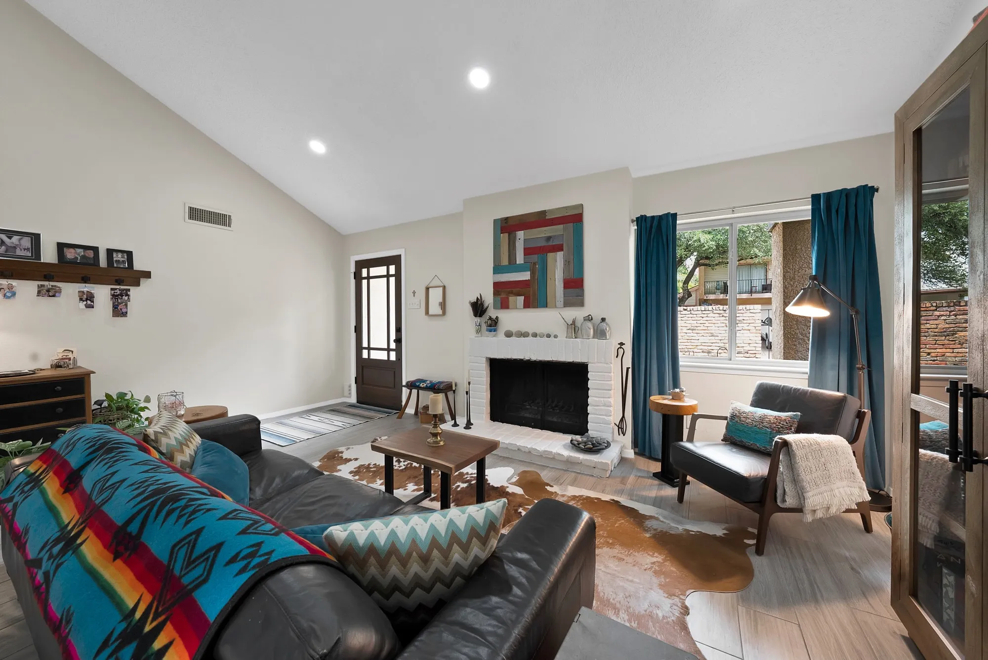 Living room — White brick fireplace with vaulted ceiling, large window, and open sightline to entry door.