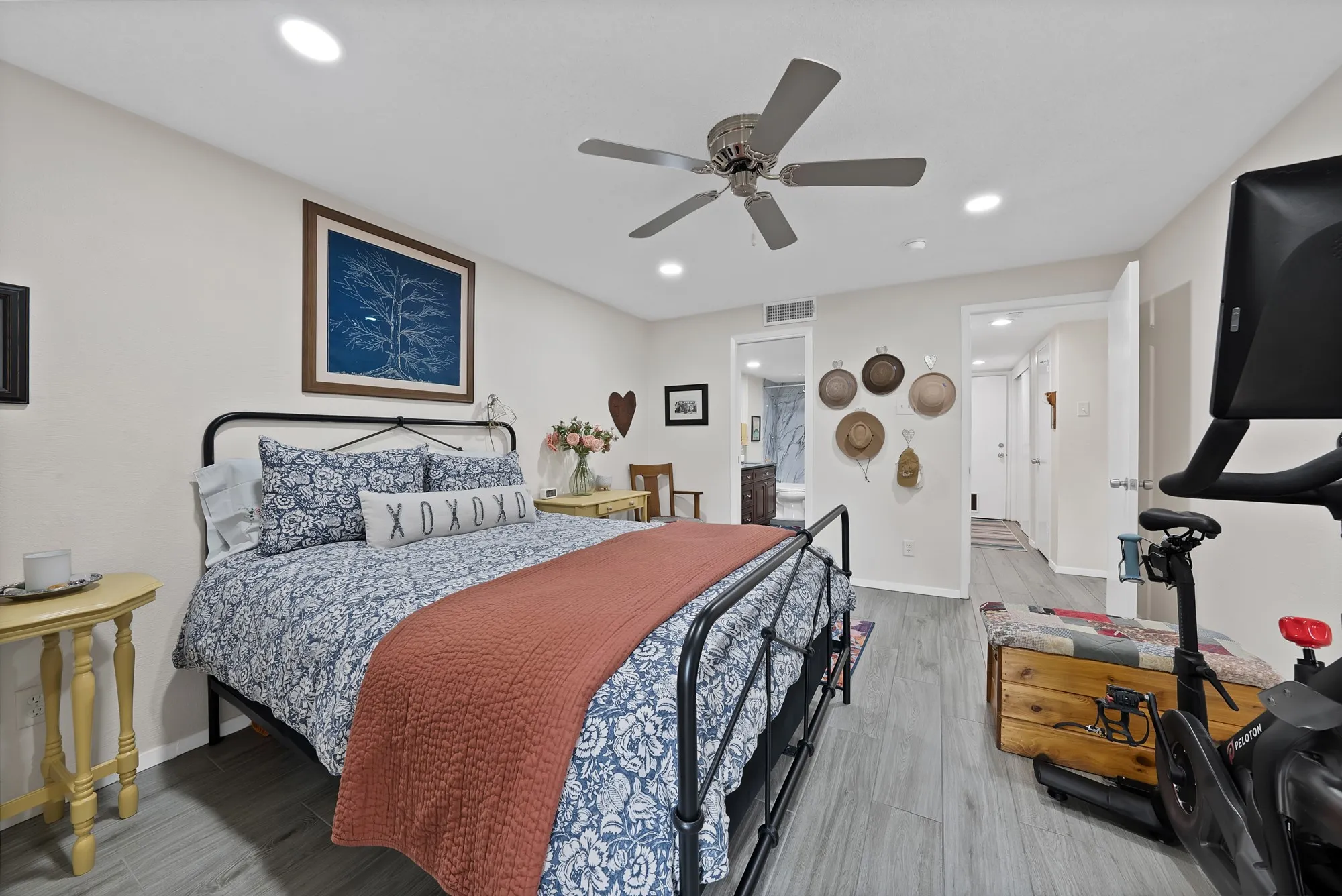 Primary bedroom — Wood look tile flooring, ceiling fan, and doorway to en suite bathroom with marble finishes visible.