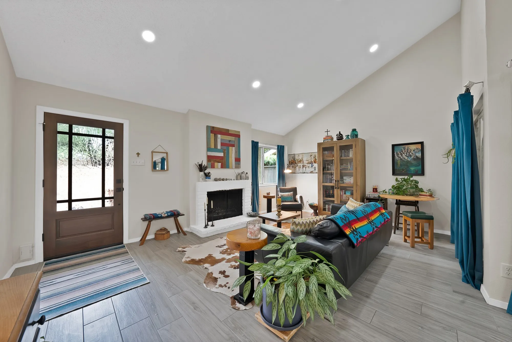 Living room — Vaulted ceiling living space with white brick fireplace, glass front bookcase, and wood look tile flooring.