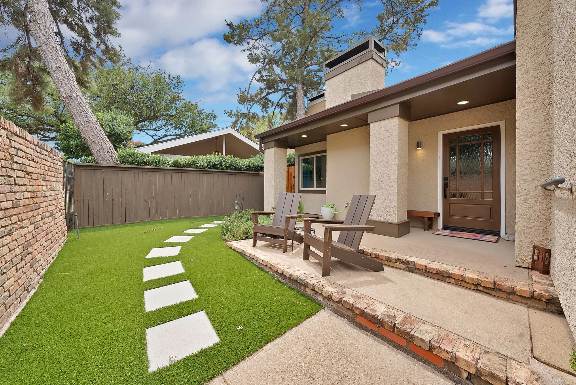 Front porch — Covered entry with paneled glass front door, brick planter border, turf lawn, and paver stepping stone path.