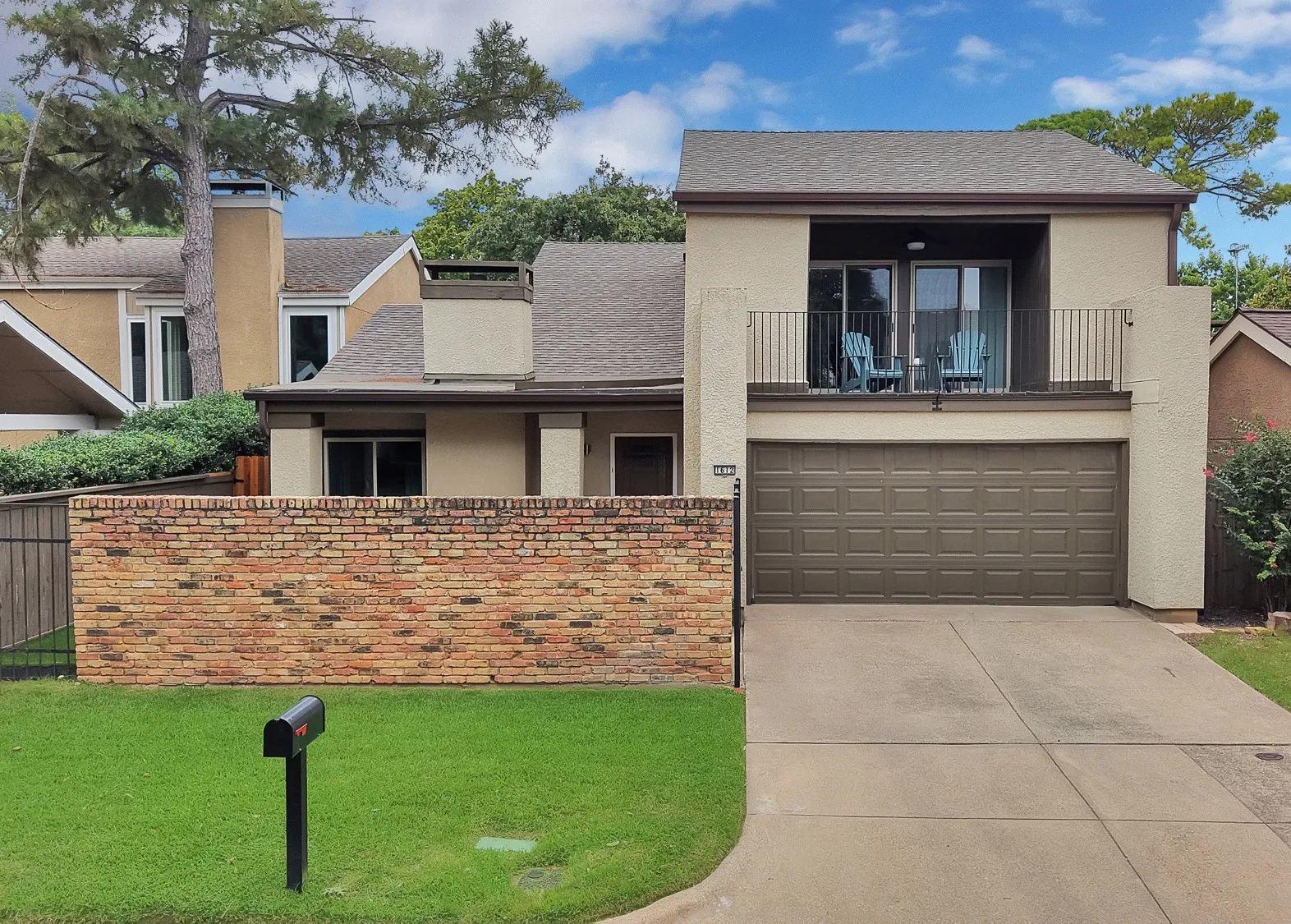 Front exterior — Gated brick courtyard entry with wrought iron gate leading to front porch, second floor balcony above garage.